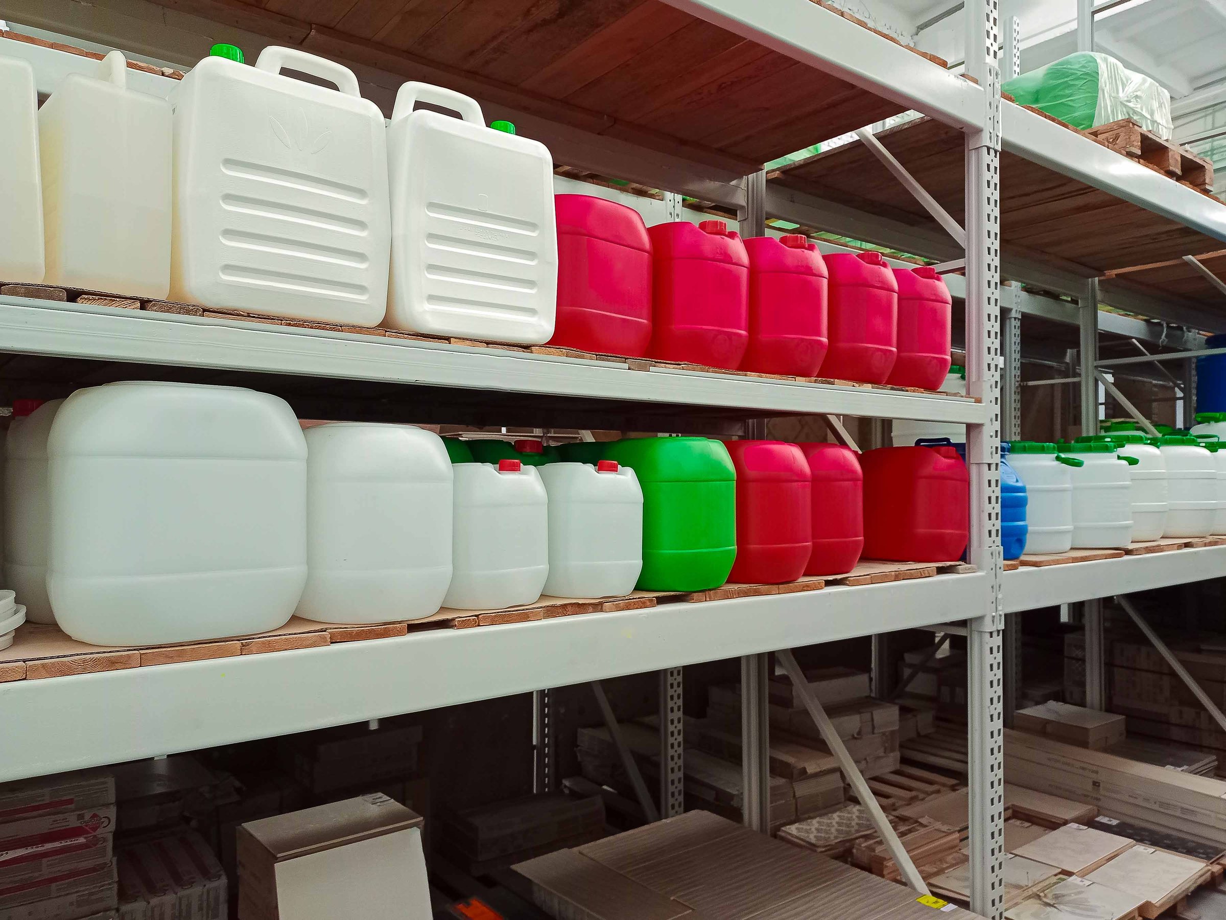 Various colored plastic storage containers neatly arranged on industrial warehouse shelves, used for liquid storage, transportation, and industrial purposes.