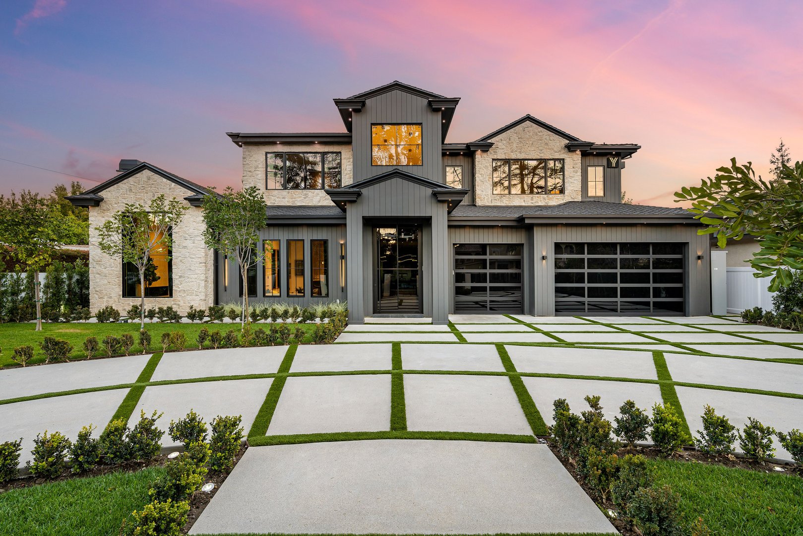 Modern luxury home with a large driveway and a beautifully landscaped front yard at sunset