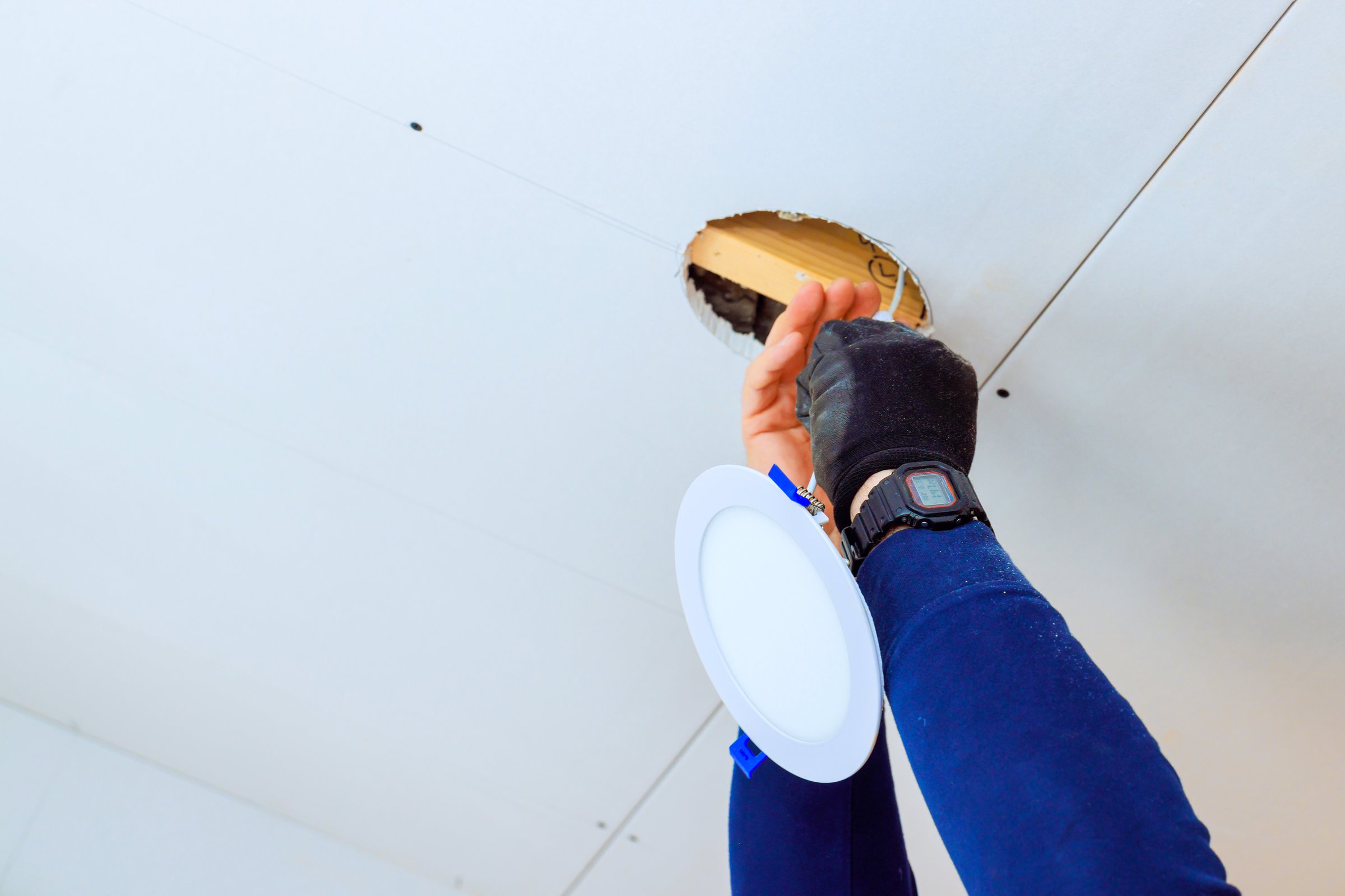 Skilled worker attaches lighting fixture inside ceiling hole, showcasing home improvement effort in progress.