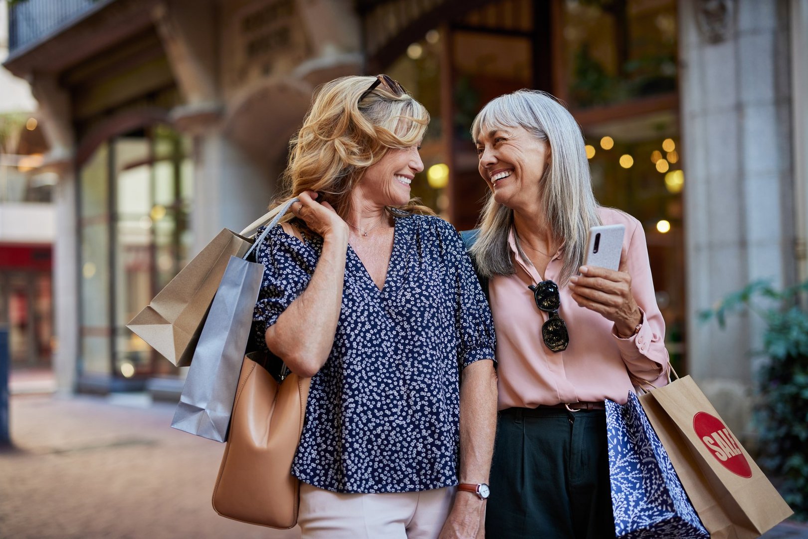 Two older beautiful women smiling after shopping together. Senior smiling ladies carrying shopping bags while laughing together. Two mature women enjoy a cheerful shopping day with a big smile.