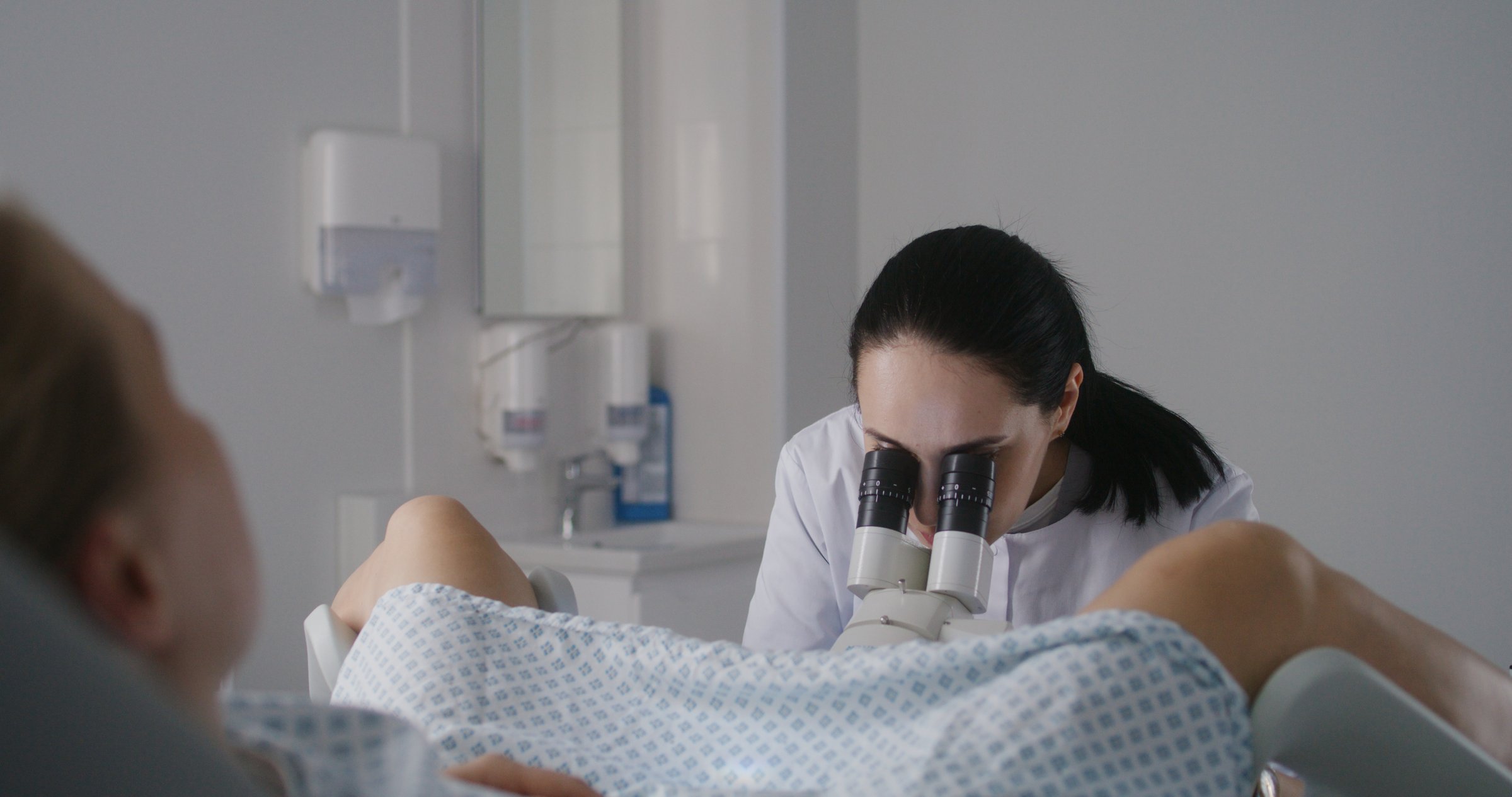 Gynecology room in modern clinic. Female gynecologist uses colposcope, takes tests from patient. Woman lies on gynecological chair during colposcopy procedure. Preparation for pregnancy. Slow motion.