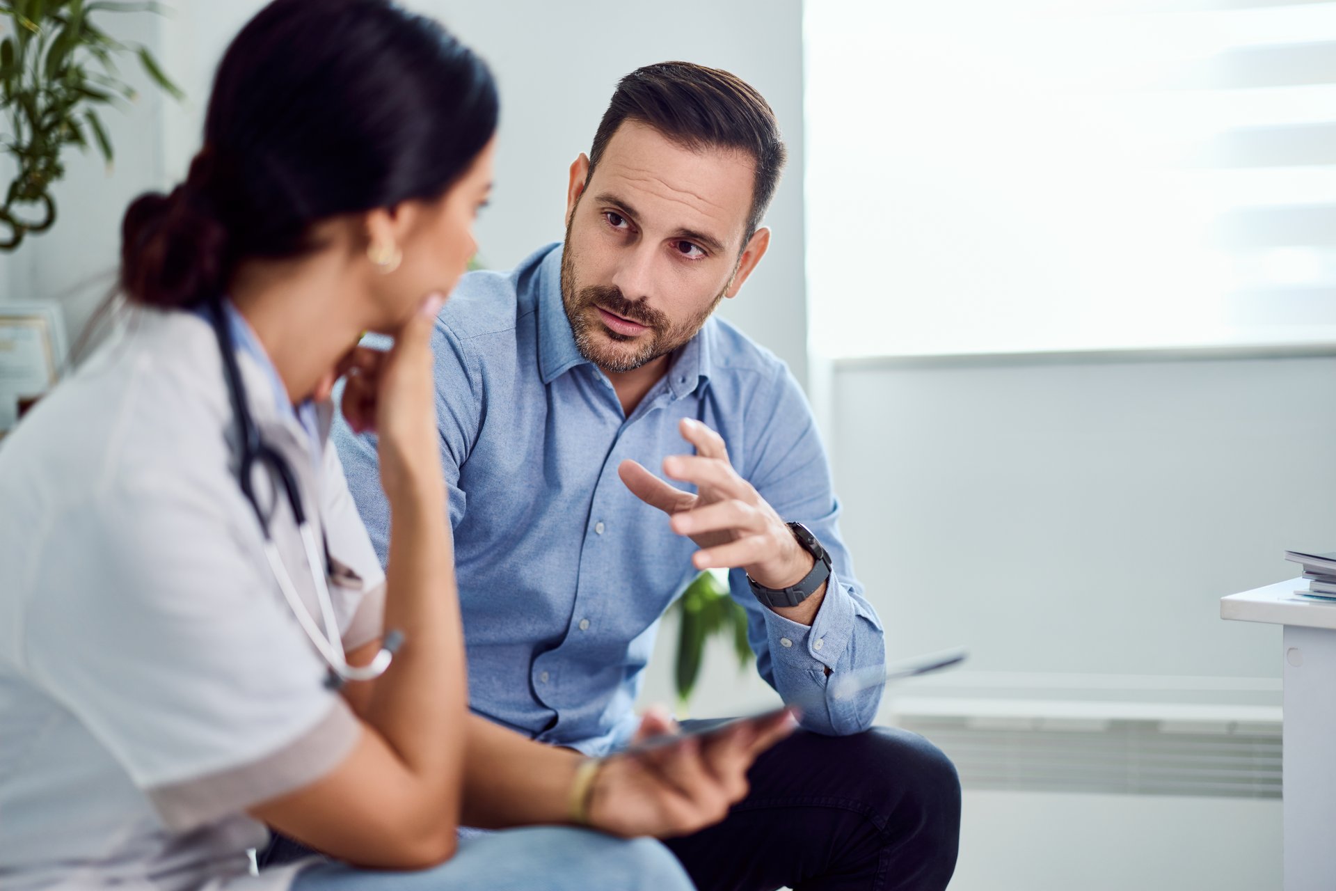 A healthcare professional and patient engaged in a conversation inside a brightly lit office. The environment suggests a professional setting aimed at communication and understanding for medical guidance.