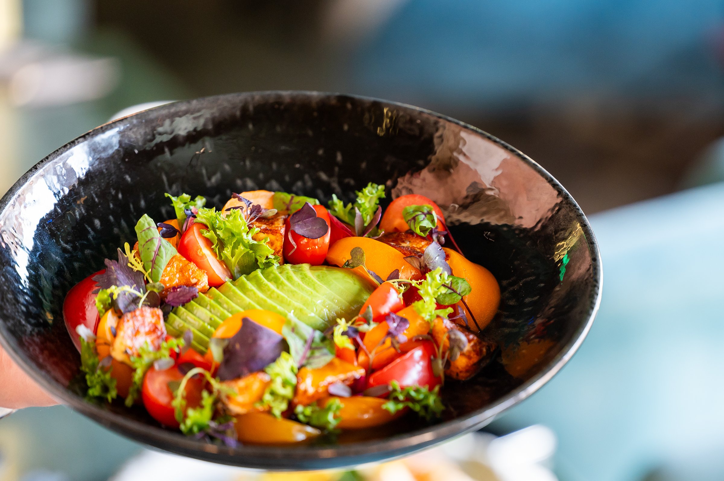 Fresh and colorful salad with avocado, cherry tomatoes, mixed greens, and grilled vegetables in a black bowl, garnished with microgreens. Healthy, vibrant, and appetizing composition