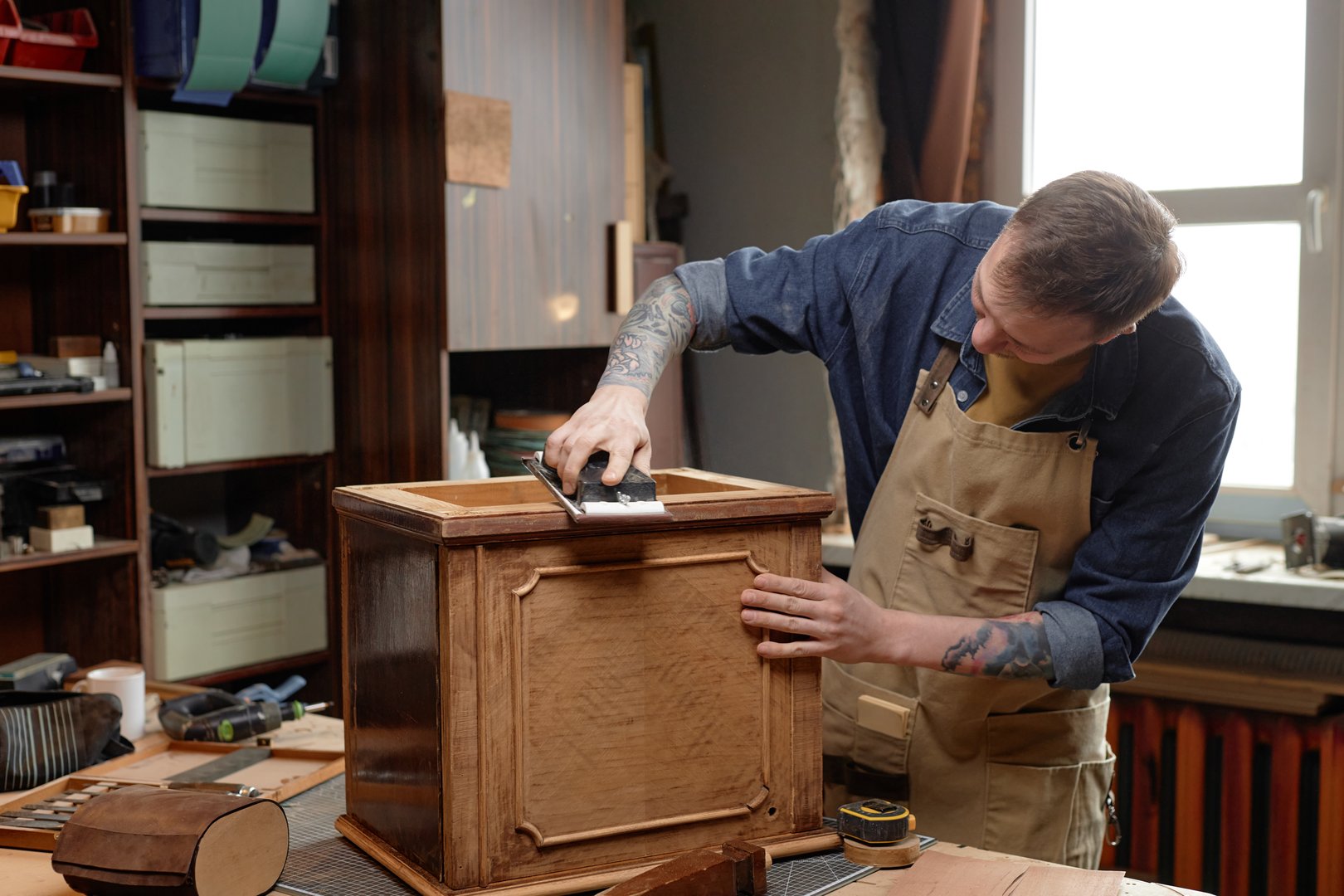 Artisanal woodworker meticulously sanding wooden cabinet in cozy, well-lit workshop, showcasing smooth craftsmanship and attention to detail with assorted tools on workbench