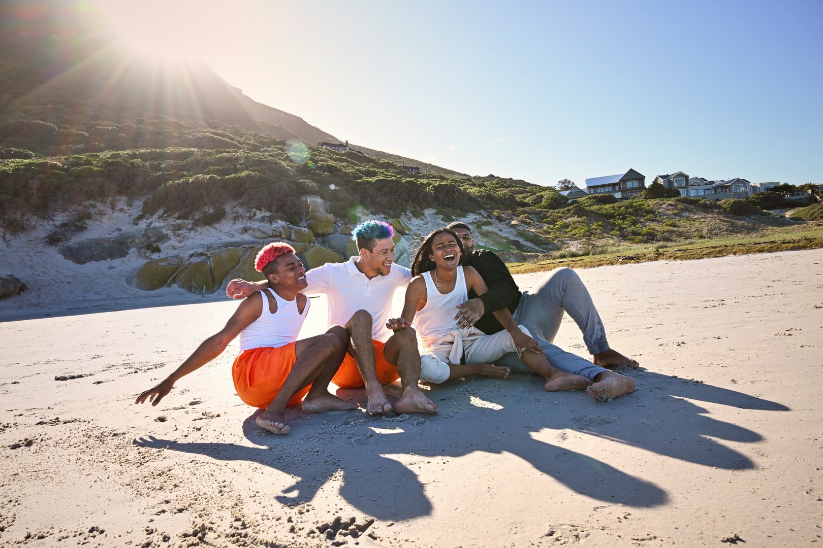 Group of friends sitting and laughing on beach on sunny day