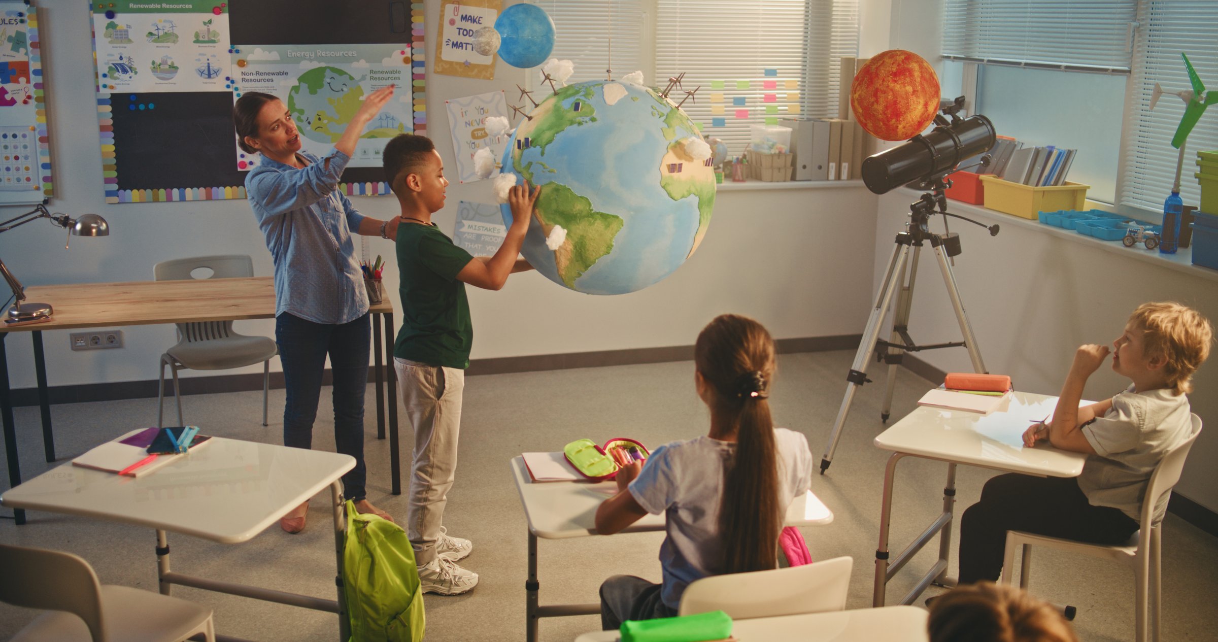 STEM Class: Female Teacher Teaches Science to Elementary School Kids in Classroom. Schoolchildren Raising Hands, African American Boy Presenting Renewable Energy Sources Using Planet Model. Dolly Shot