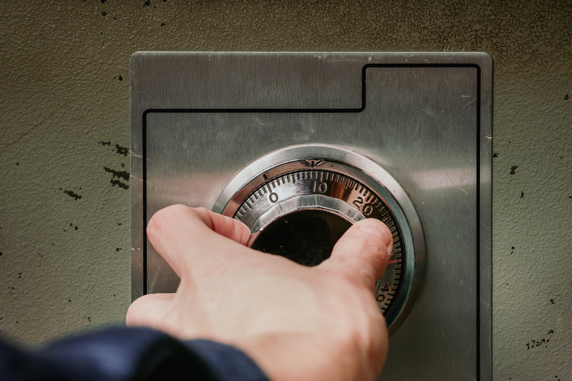 Woman turning wheel combination lock with analog numbers. Close up of old fire proof steel safe. Selective focus.