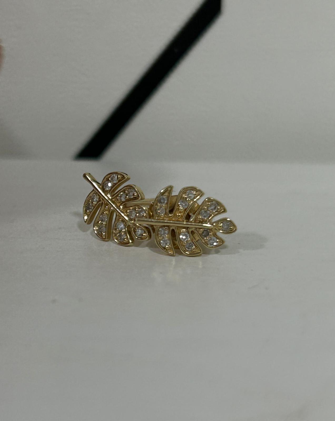 Gold leaf-shaped earrings with embedded clear gemstones on a white surface.