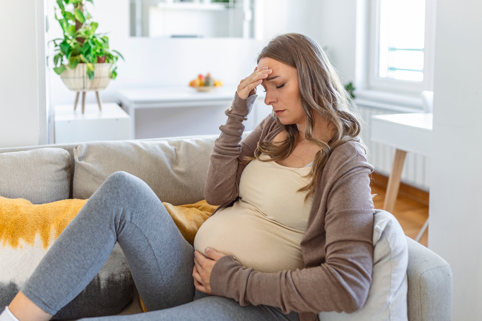 pregnant young adult woman resting on sofa at home, feeling unwell. Young pregnant woman has suffered from headaches sitting on the sofa. Pregnancy symptoms