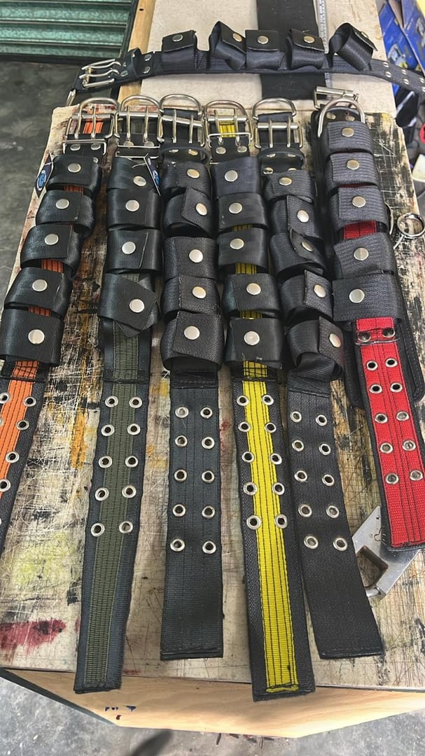 Colorful fabric belts with metal grommets and black padding, arranged side by side on a wooden surface.