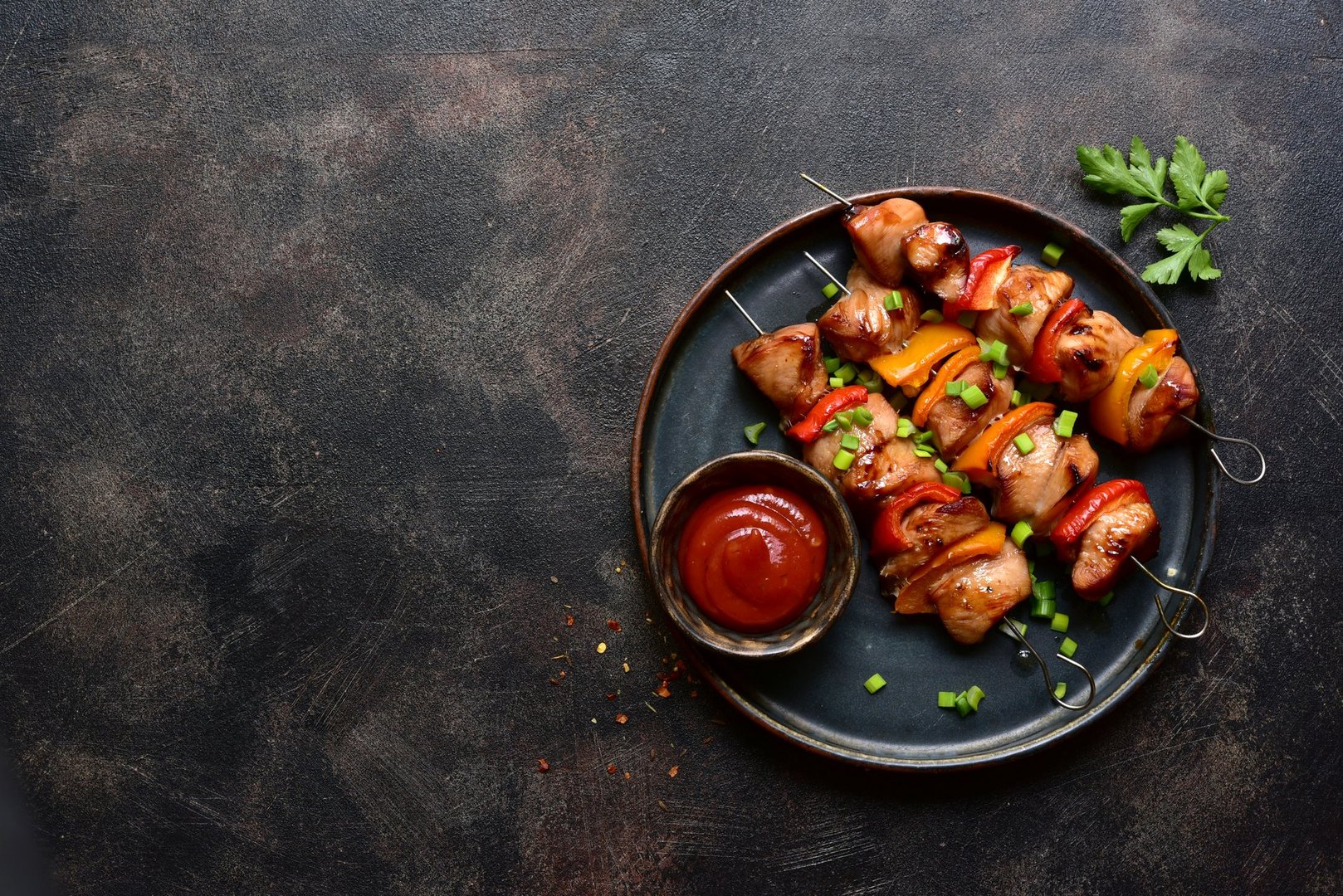 Grilled chicken kebab on a plate over dark metal tray. Top view with copy space.