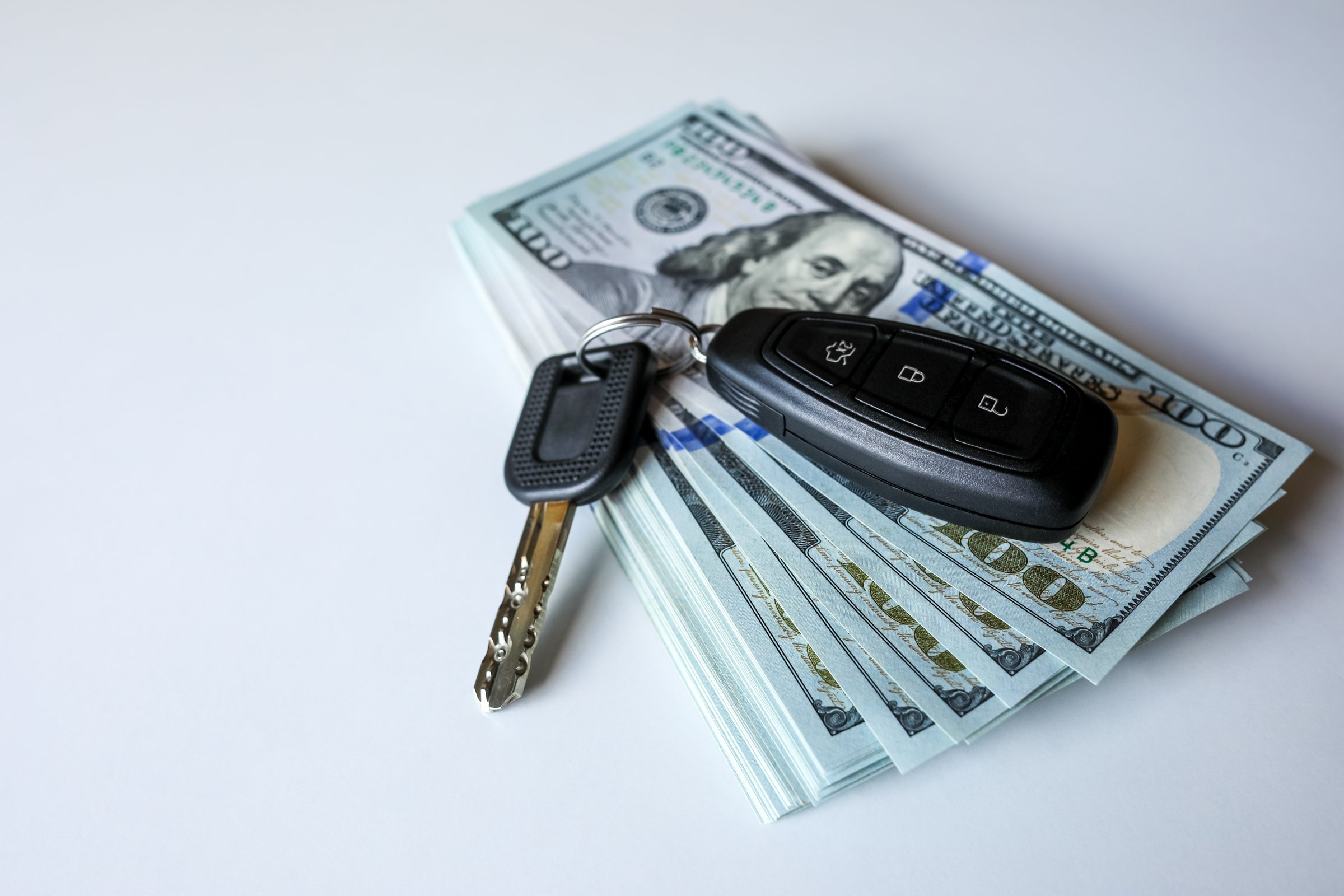 Car keys placed on a heap of hundred-dollar bills represent luxury, financial achievement, and high-value spending. Ideal for visuals related to auto loans, wealth, or premium purchases.