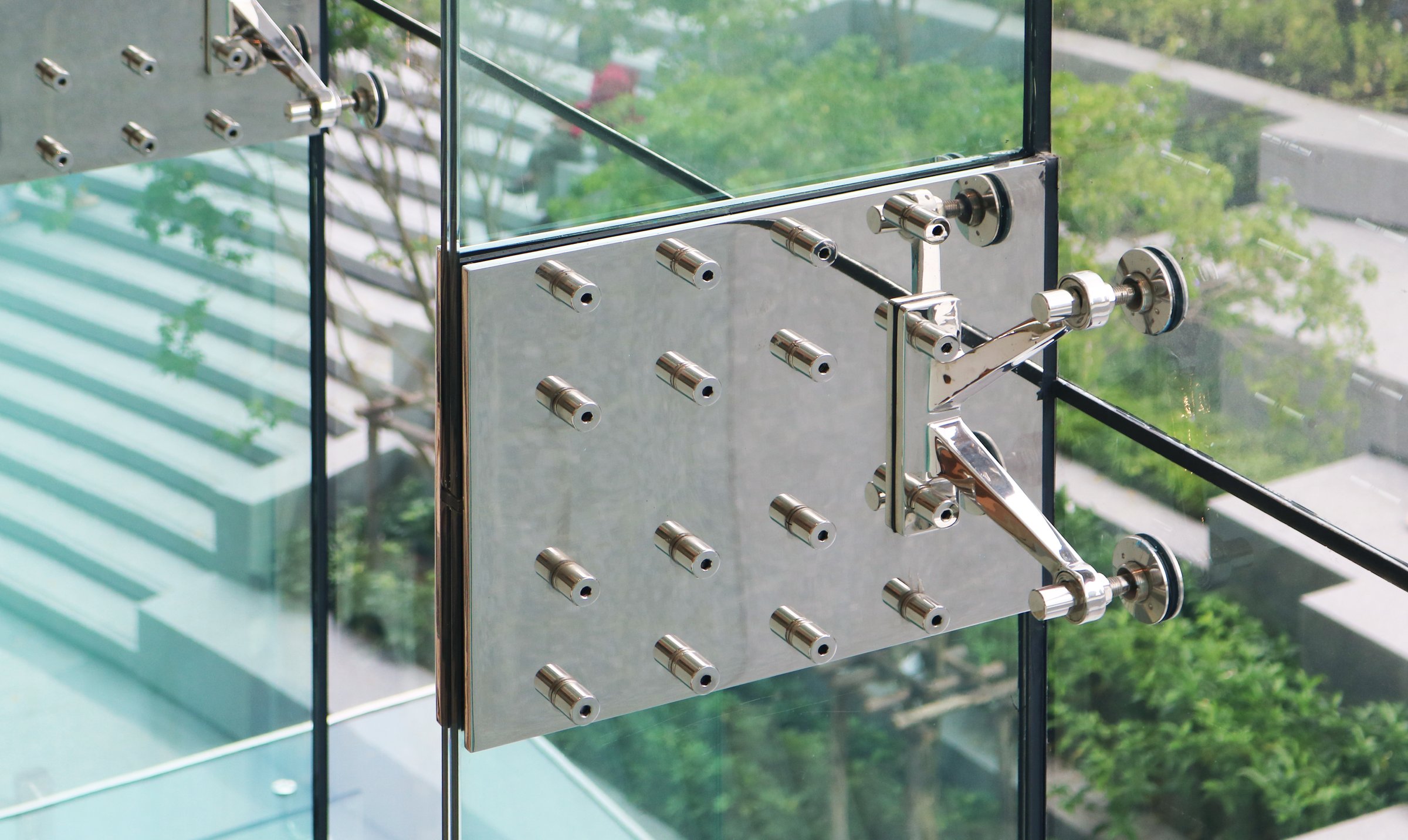 Stainless steel glass fin splice plate with spider fittings installed on vertical glass rib structure wall.