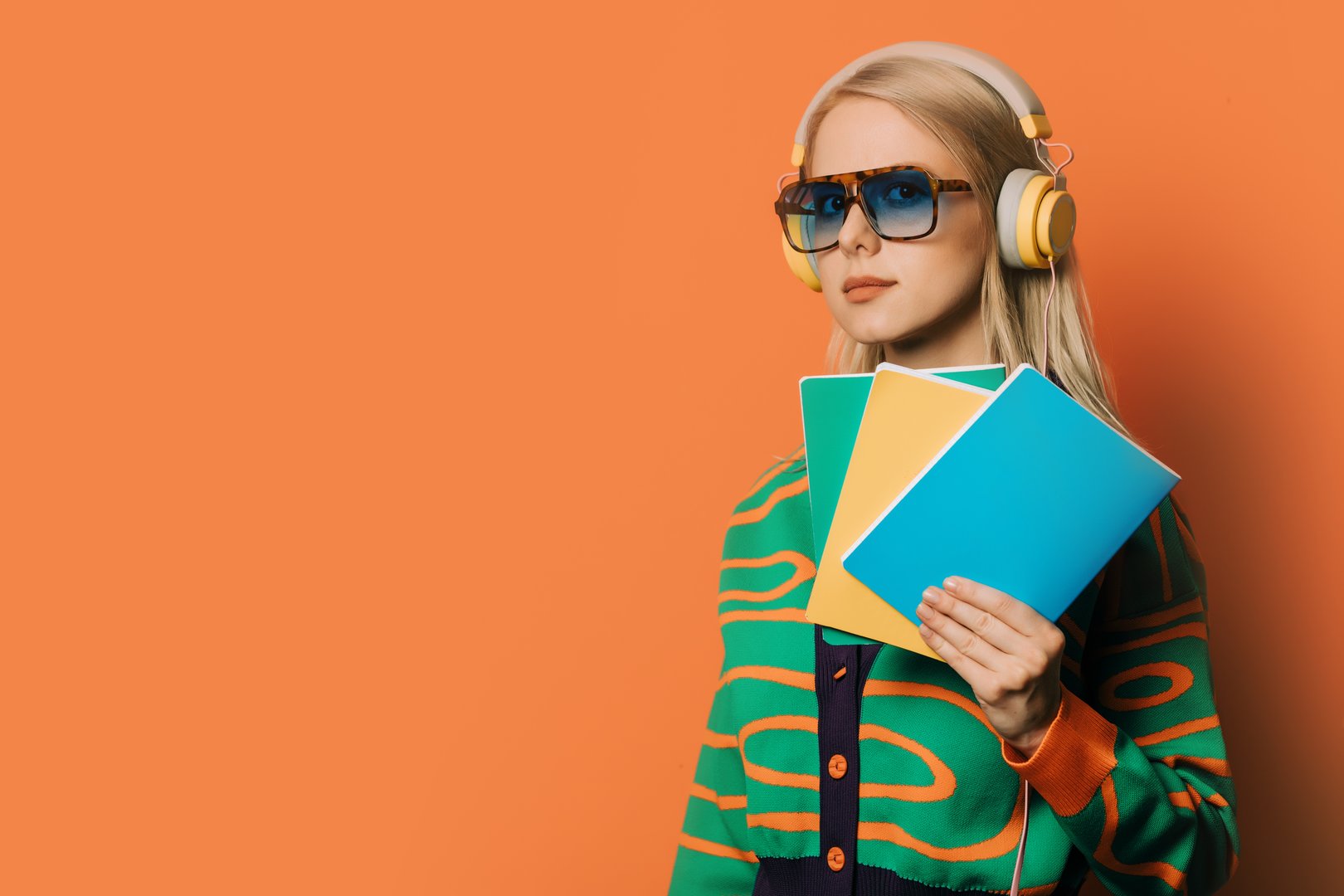 Stylish 80s woman in eyeglasses and headphones with notebooks on orange background