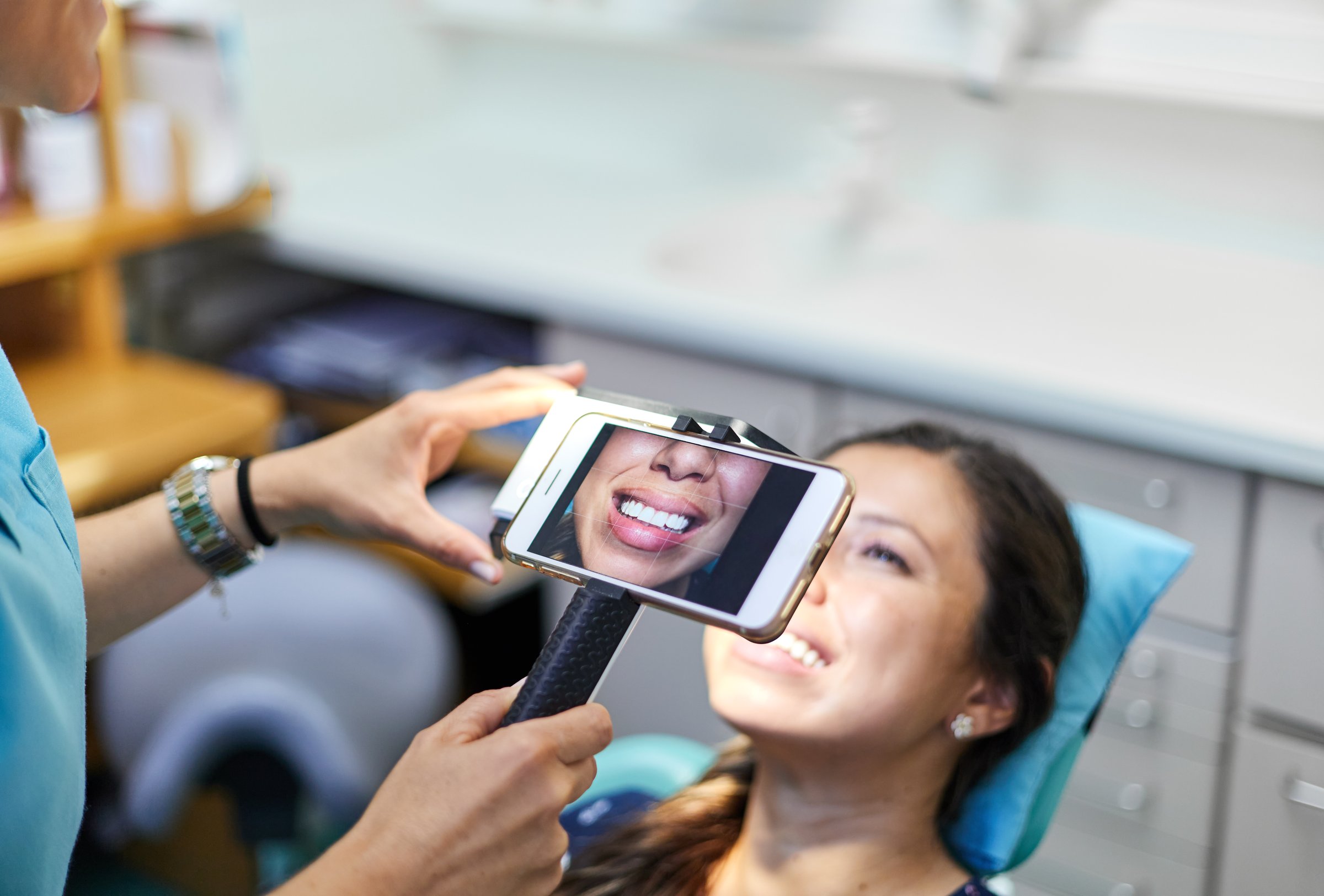 From above soft focus of crop dentist using smartphone on monopod to take photo of female patient smile for portfolio during appointment in office of dental clinic