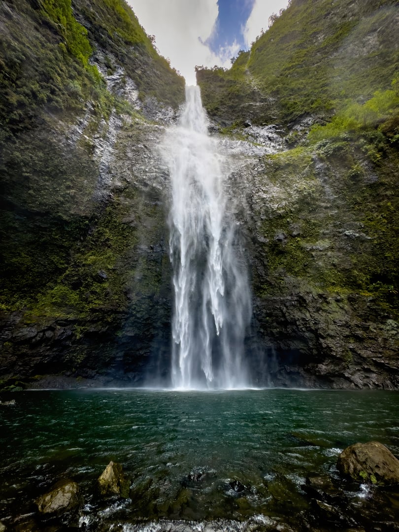 Scenic view of Hanakapiai Falls, a waterfall at the end of Hanakapiai Valley hiking trail, Kauai, Hawaii, USA against blue sky with clouds