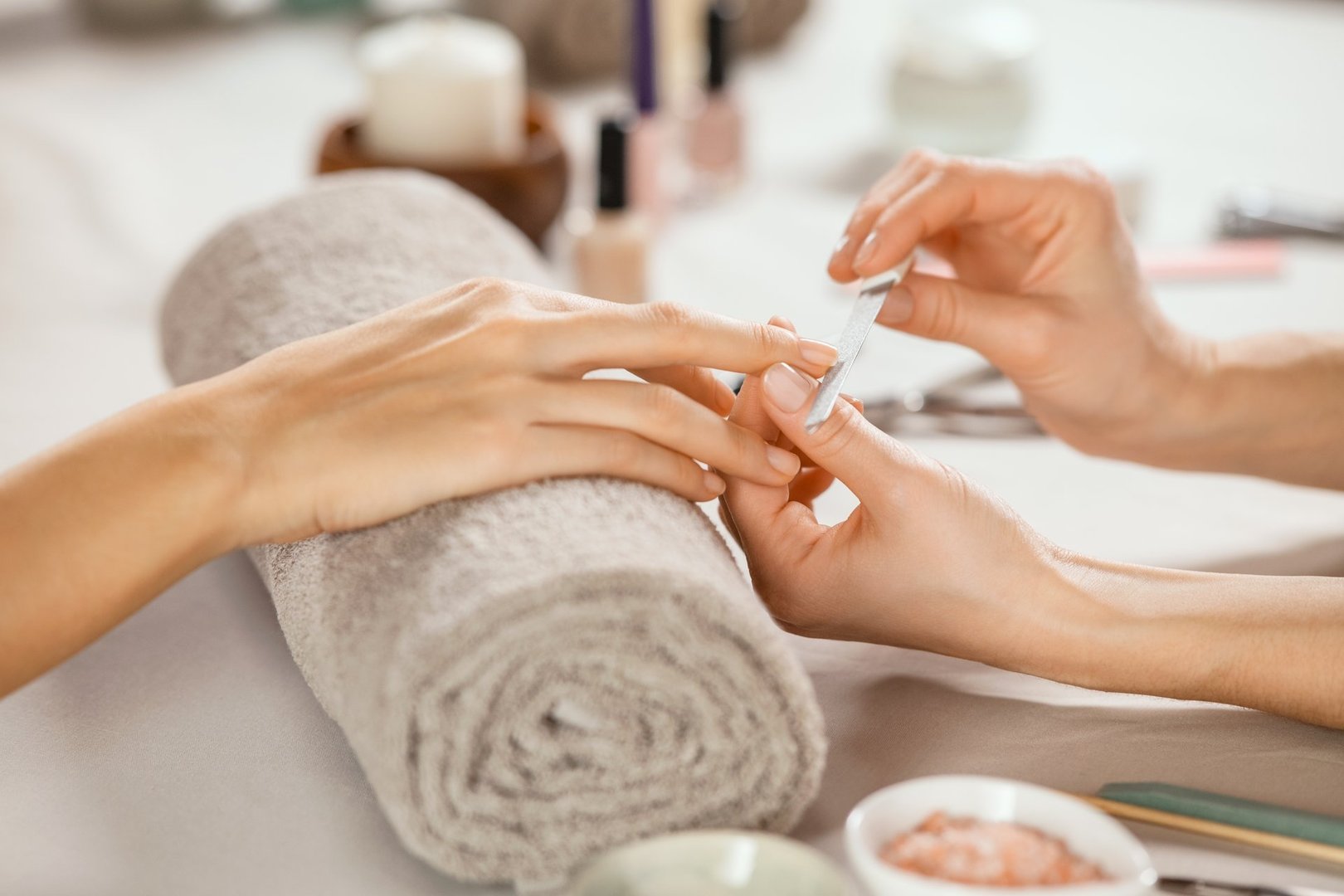 Close up shot of a woman in a nail salon receiving manicure by beautician with metal nail file. Woman getting nail manicure at spa centre. Beautician file nails to a customer in luxury salon.