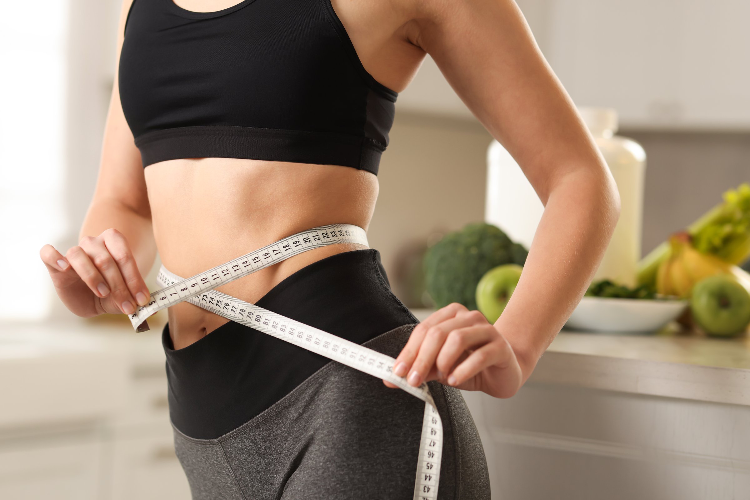 Weight loss. Woman measuring waist with tape in kitchen, closeup