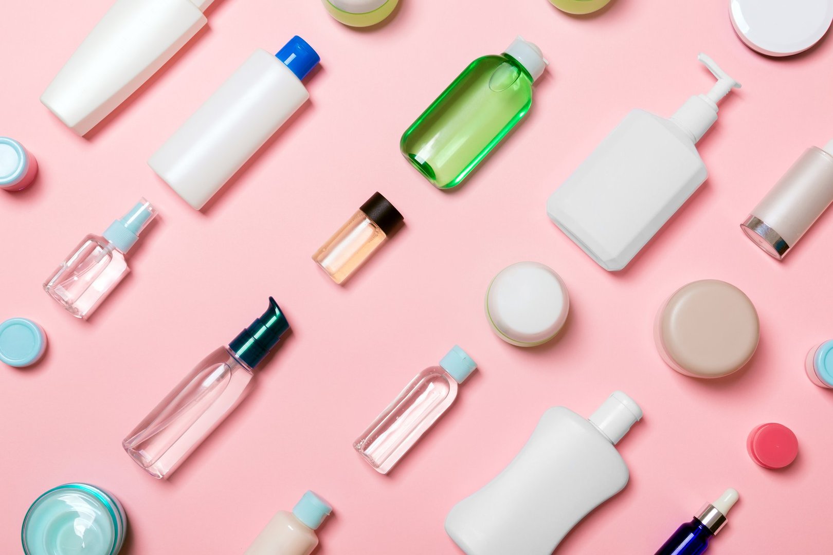 Top view of different cosmetic bottles and container for cosmetics on pink background. Flat lay composition with copy space.