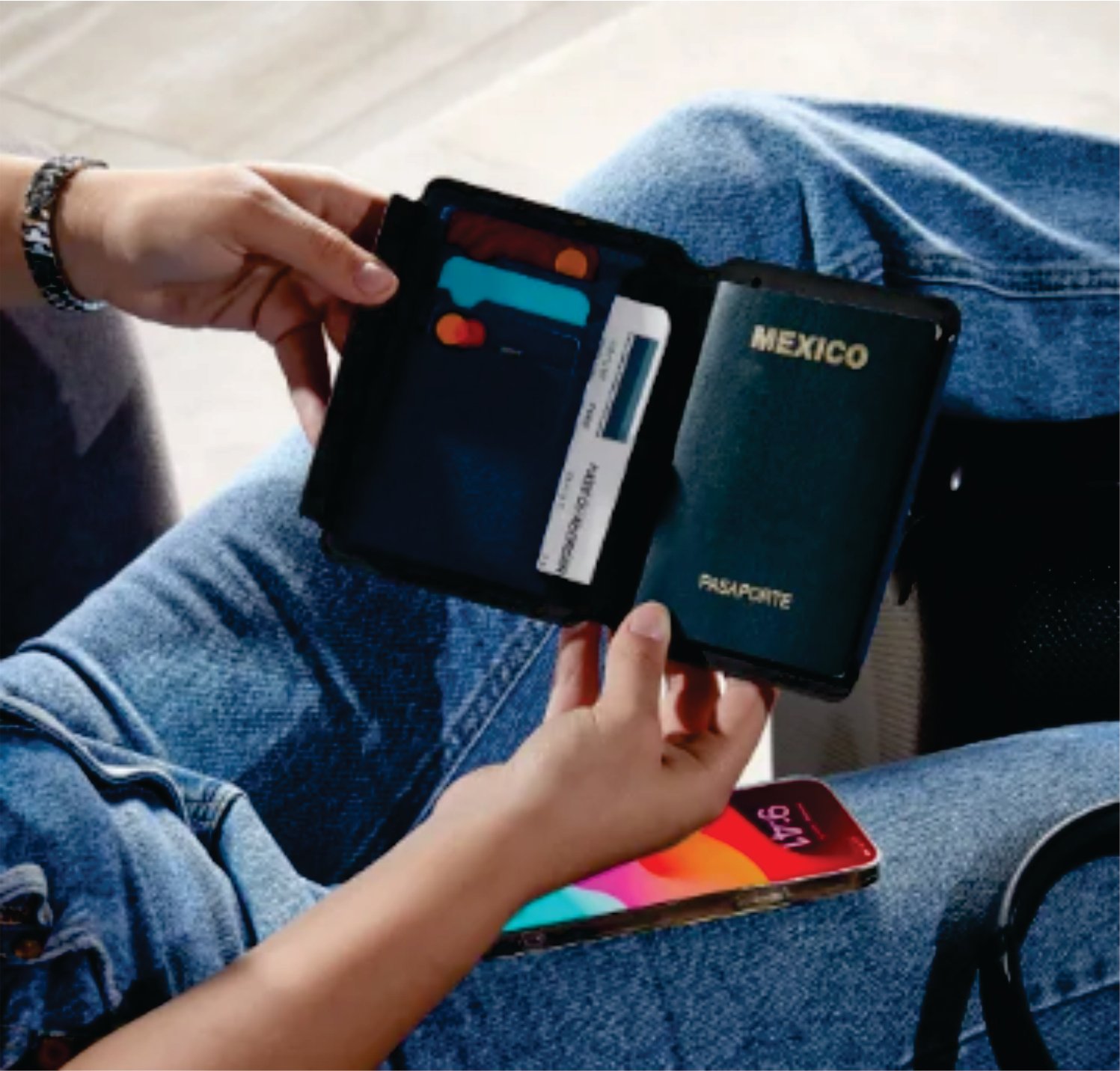 Person holding a black wallet containing a Mexican passport and cards, with a smartphone nearby on their lap.