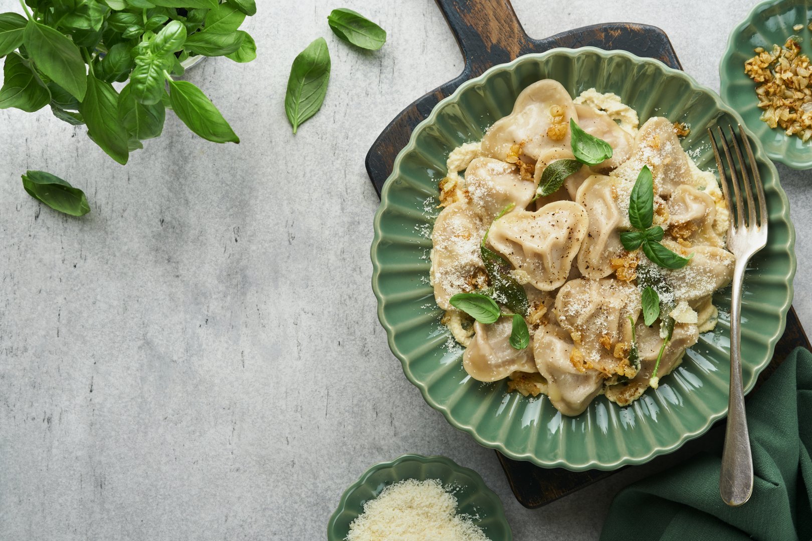 Homemade italian ravioli pasta in heart shape with beef meat, cheese butter sauce, caramelized onions, basil and saffron on old grey background. Food cooking menu ingredients background. Top view.