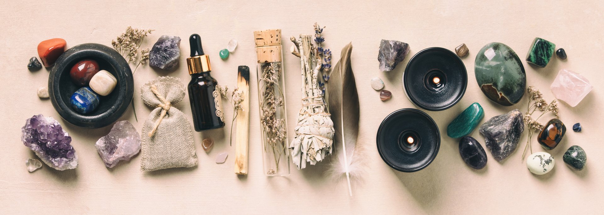 Flat lay of crystals, herbs, and candles arranged for alternative healing and wellness practices, on a light background.