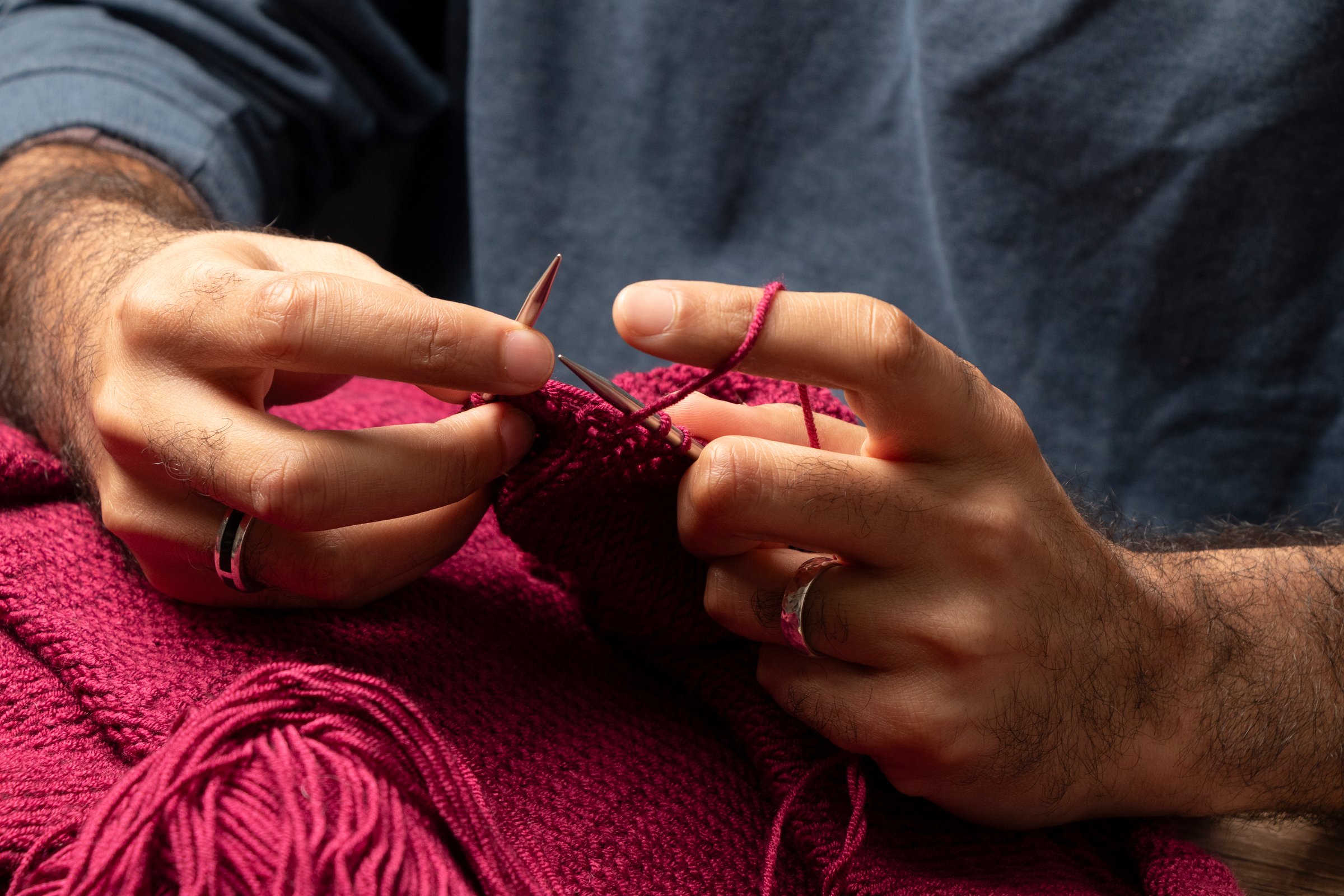 Man's hands knitting a burgundy vest with knitting needles and wool