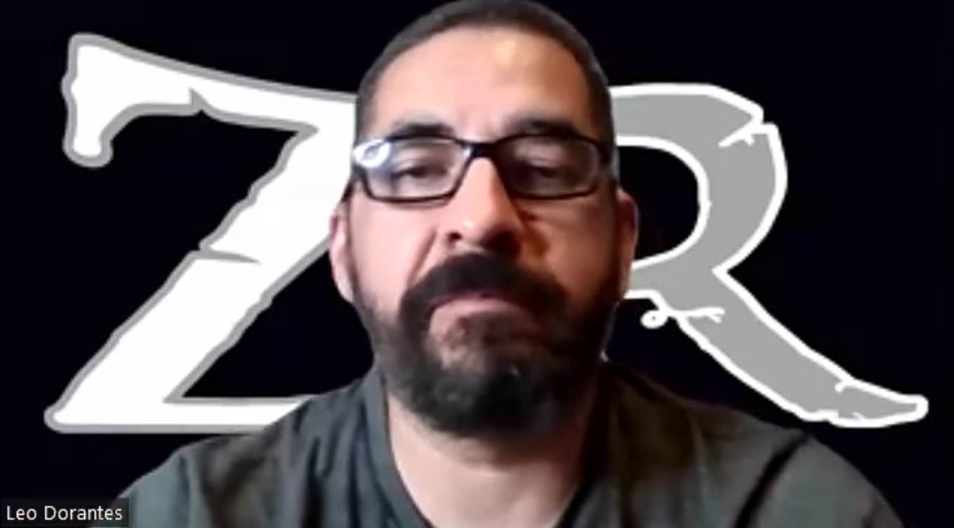 A bearded man wearing glasses is speaking on a video call, with white ZR letters on a black background behind him.