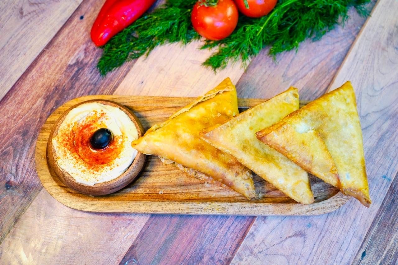 salad with colorful tomatoes, mozzarella balls, and a variety of olives, garnished with herbs, served in a bowl on a textured tablecloth with olive oil and bread