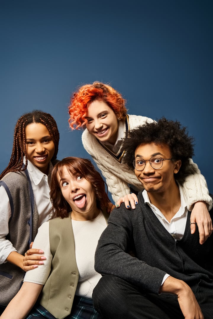 A diverse group of college students laughs and poses playfully together in a vibrant studio setting.