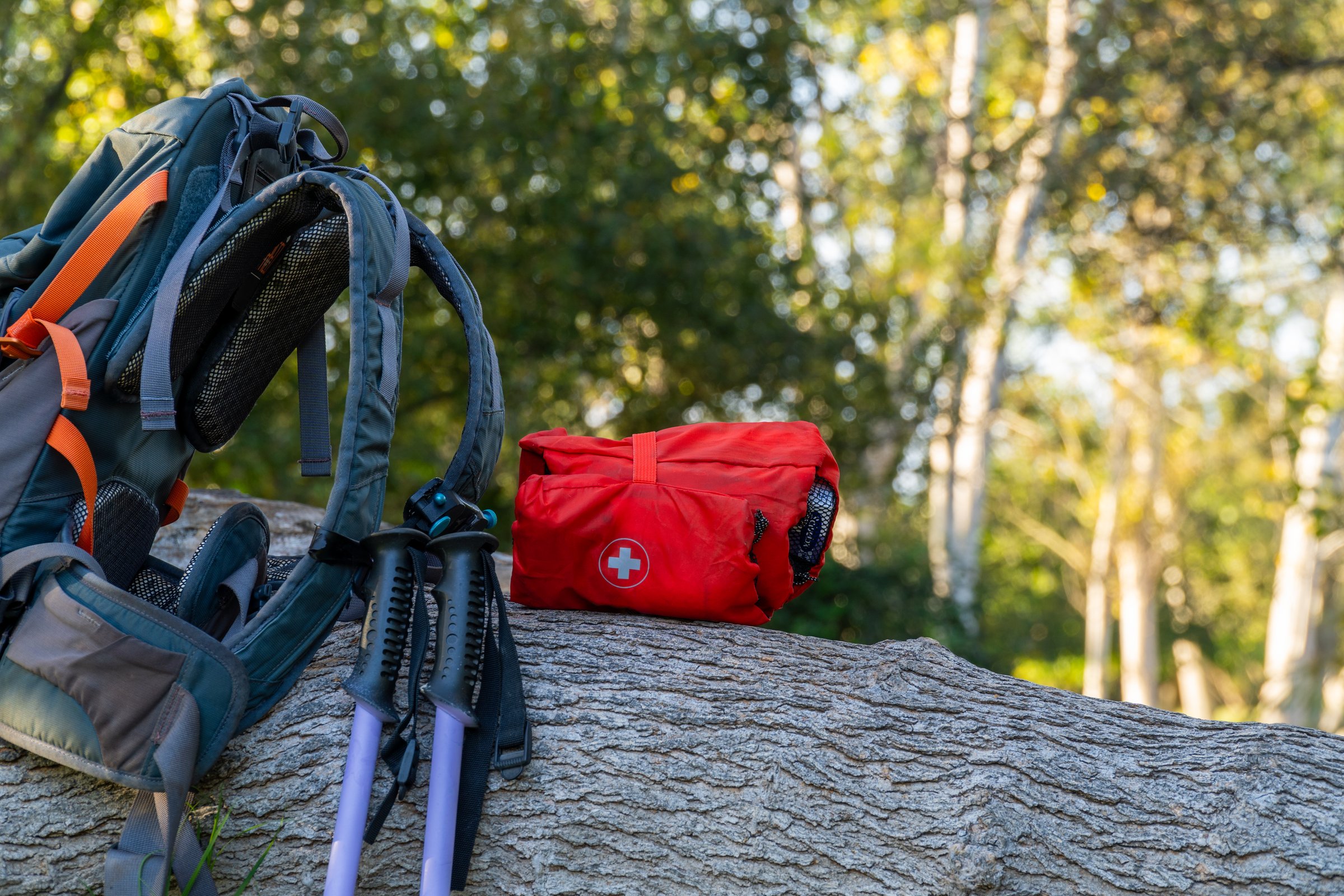 First aid kit on a log next to a hiking backpack, in a forest at sunset