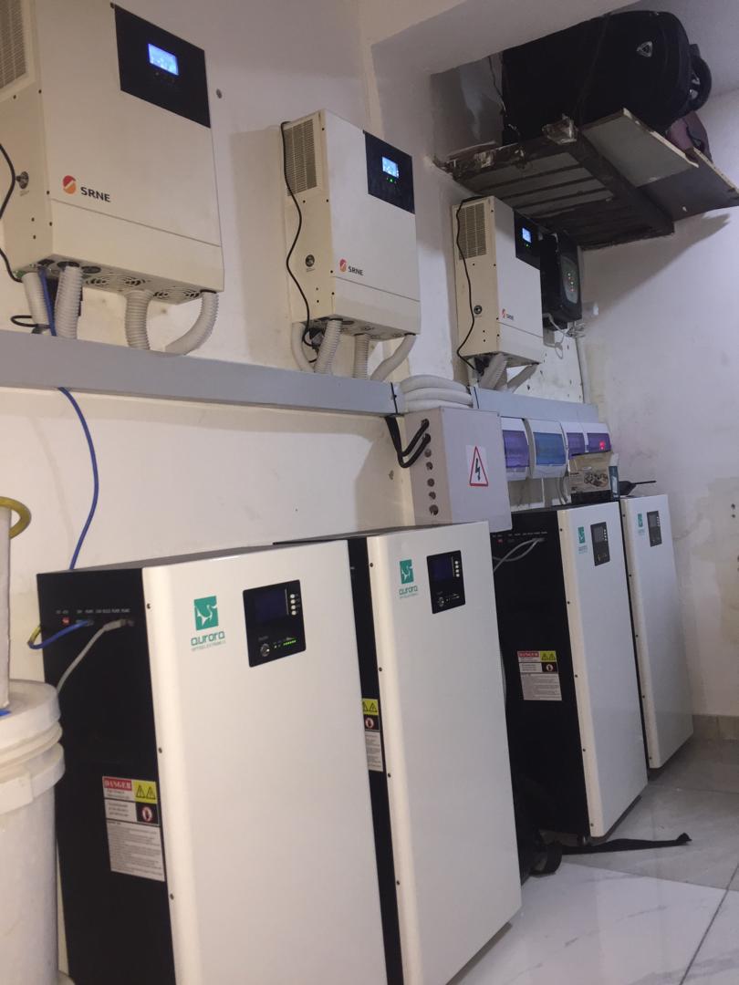 Wall-mounted inverters and floor-standing battery units in a room, part of a renewable energy system setup.