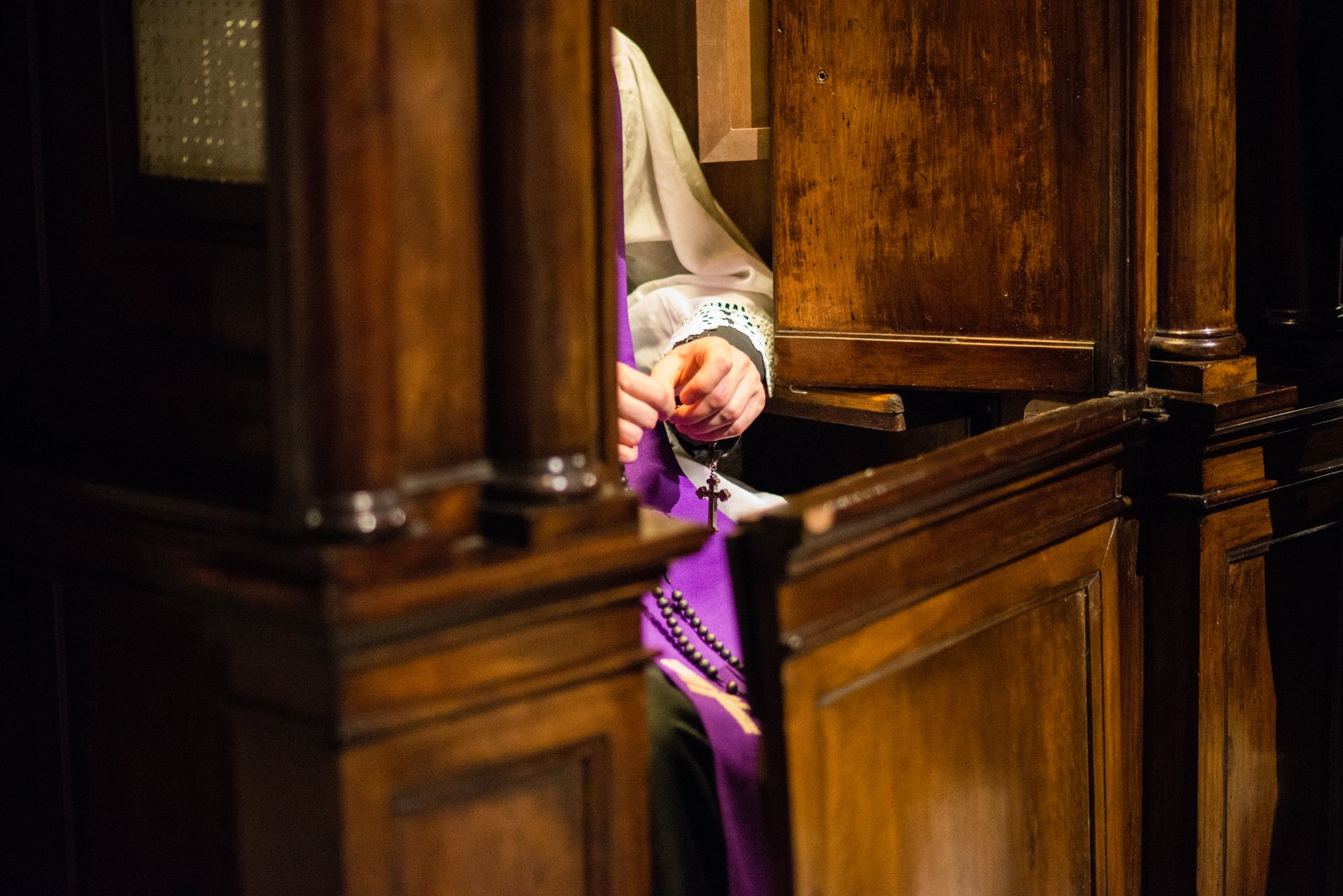priest in the confessional recites the rosary awaiting penitent