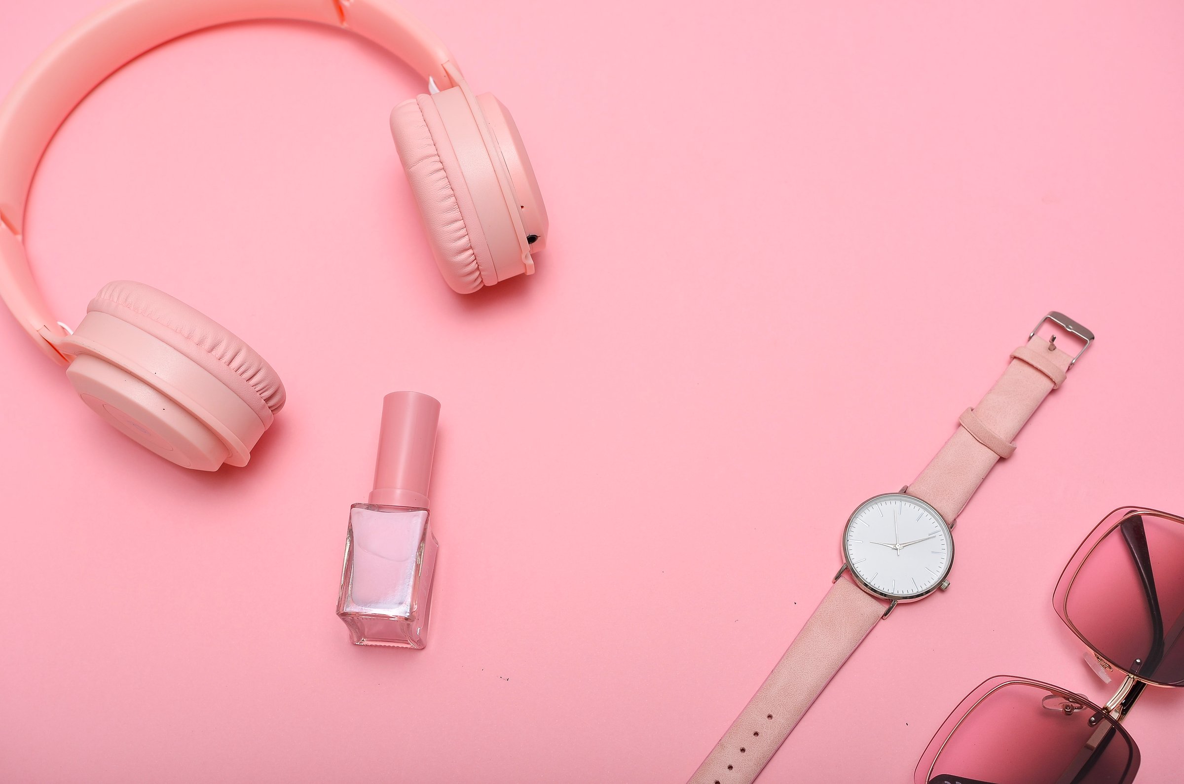 Pink headphones, nail polish, wristwatch, and sunglasses on pink background