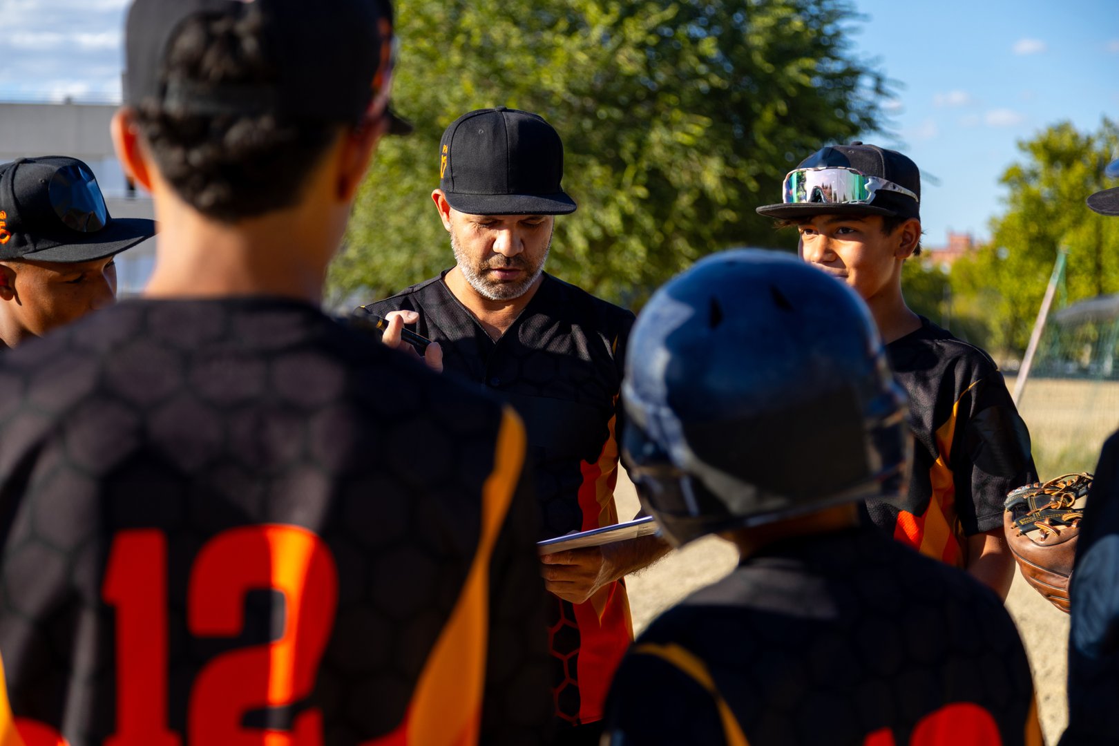 Baseball coach drawing tactics on a clipboard, discussing game strategy with young players during a huddle
