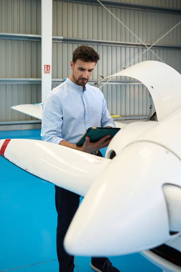 Aircraft mechanic inspecting a small plane in a hangar while using a digital tablet, demonstrating skill and precision in aviation maintenance