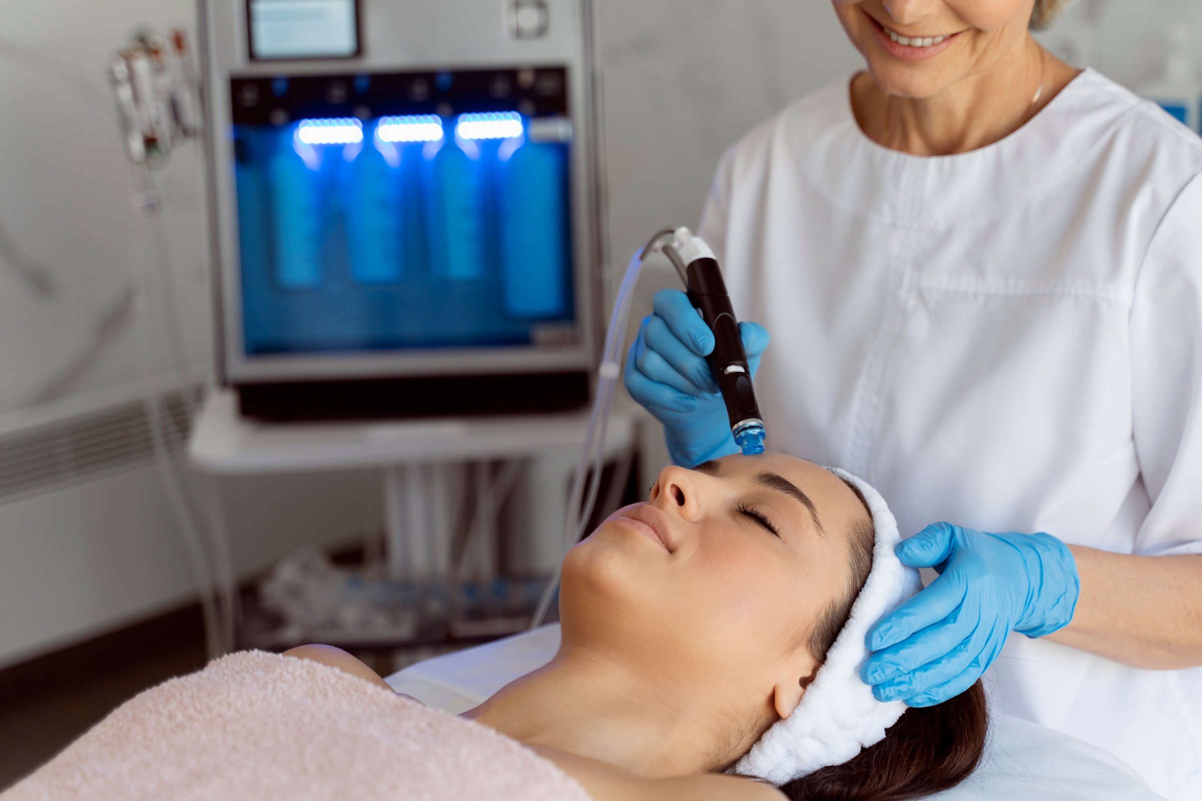 Professional female cosmetologist doing hydra-facial procedure in cosmetology clinic. Doctor using hydra vacuum cleaner. Rejuvenation and cosmetology concept