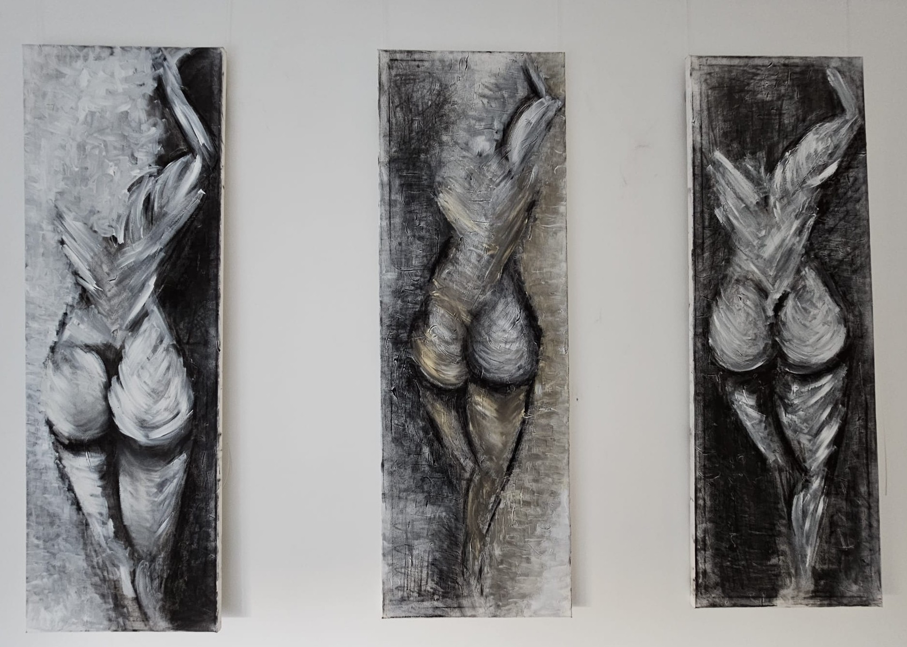 Three abstract paintings of a stylized female form in shades of black, white, and gray, displayed in a row on a wall.