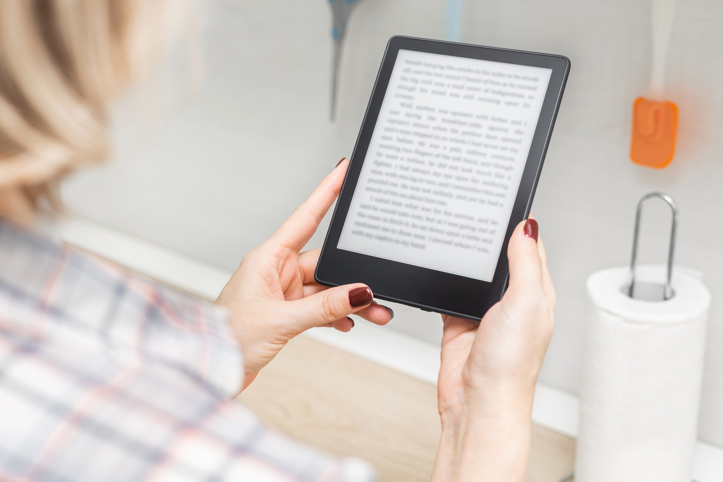 woman reading e-book in kitchen at home. housewife reading e-book. woman holding e-book in hand at home. e-ink book. ebook mockup. place for inscription