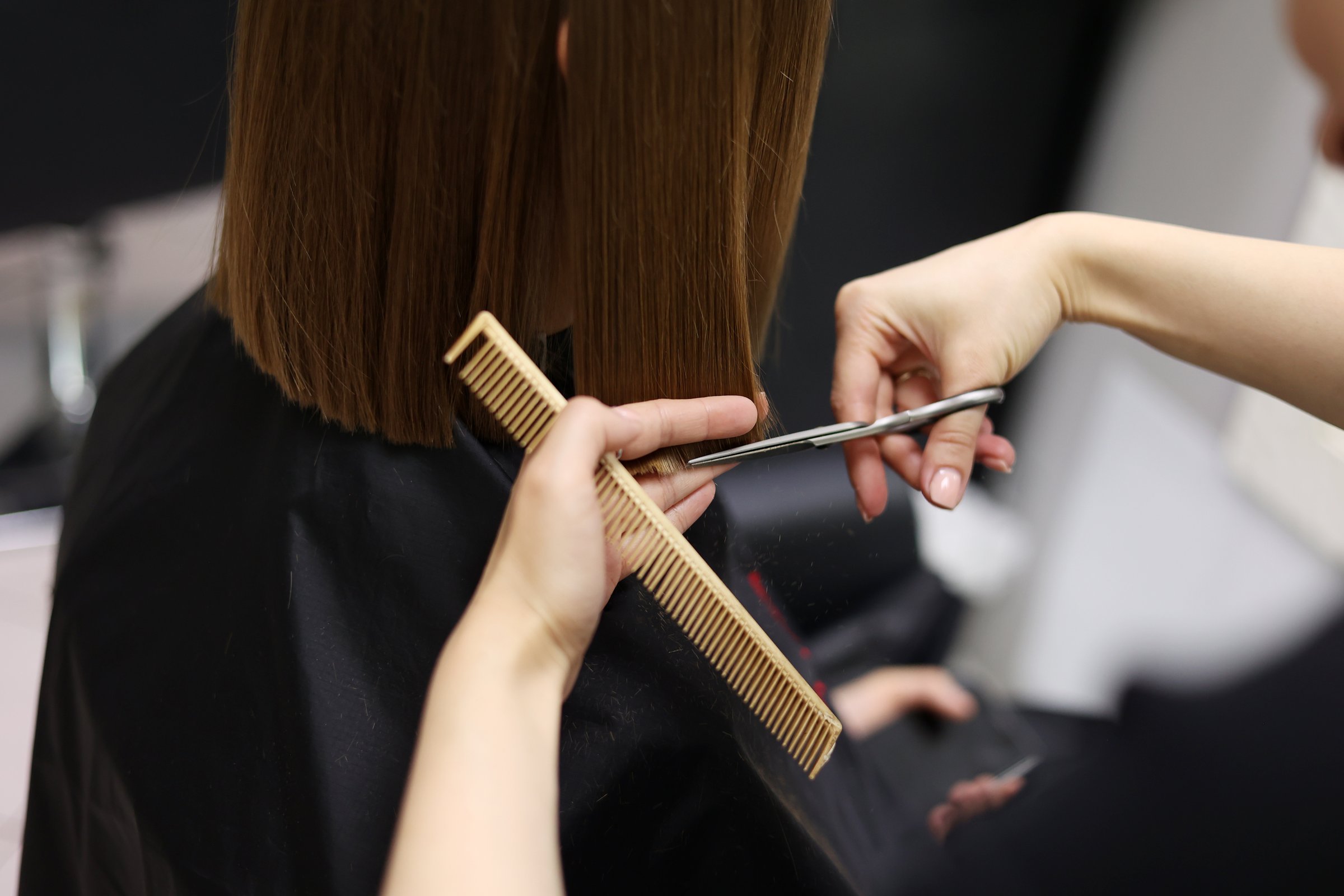 Unrecognisable hairdresser cutting female client hair with professional barber scissors and comb and making stylish haircut short bob hairstyle in beauty salon. Hair care, hair salon and hairstyling.