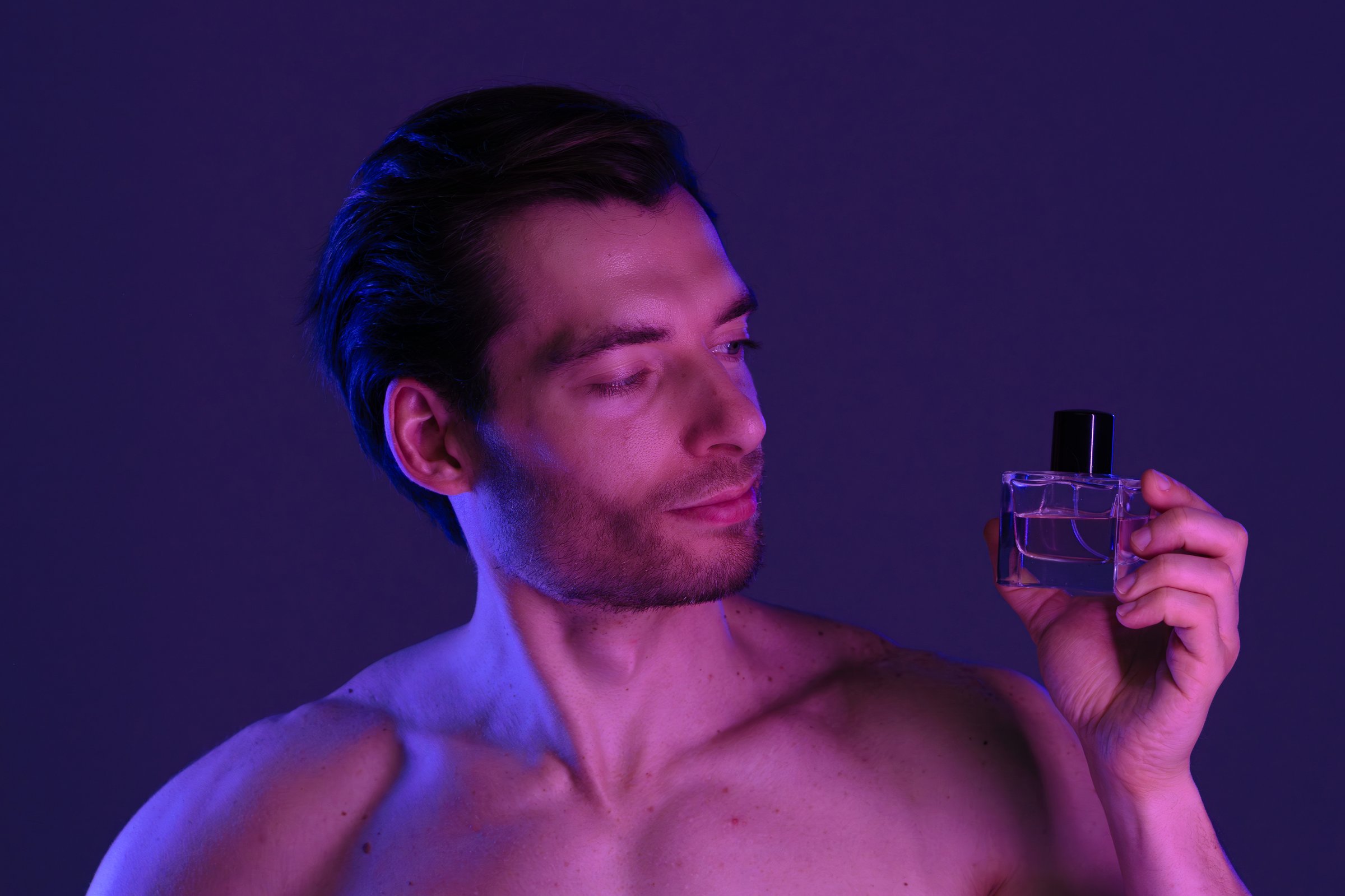 A man gazes at a perfume bottle, highlighted by blue lighting, conveying elegance and sophistication.