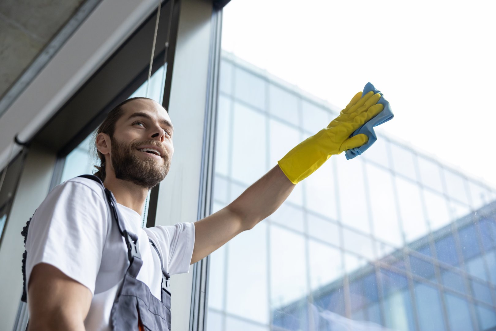 Service in the office. Young service man cleaning windows in the office and looking busy