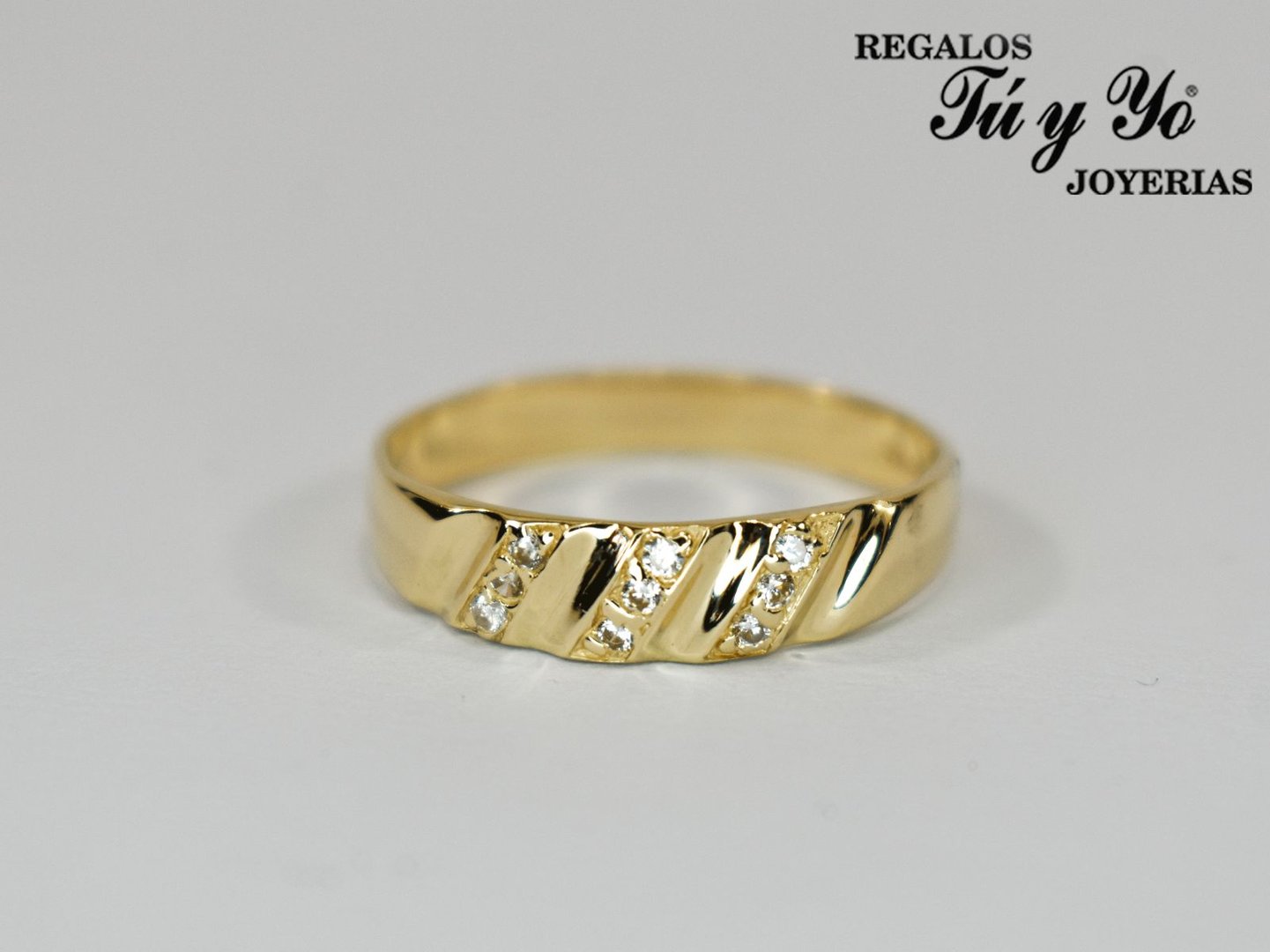 Gold ring with diagonal diamond accents, displayed on a white background. "Regalos Tú y Yo Joyerías" in top corner.