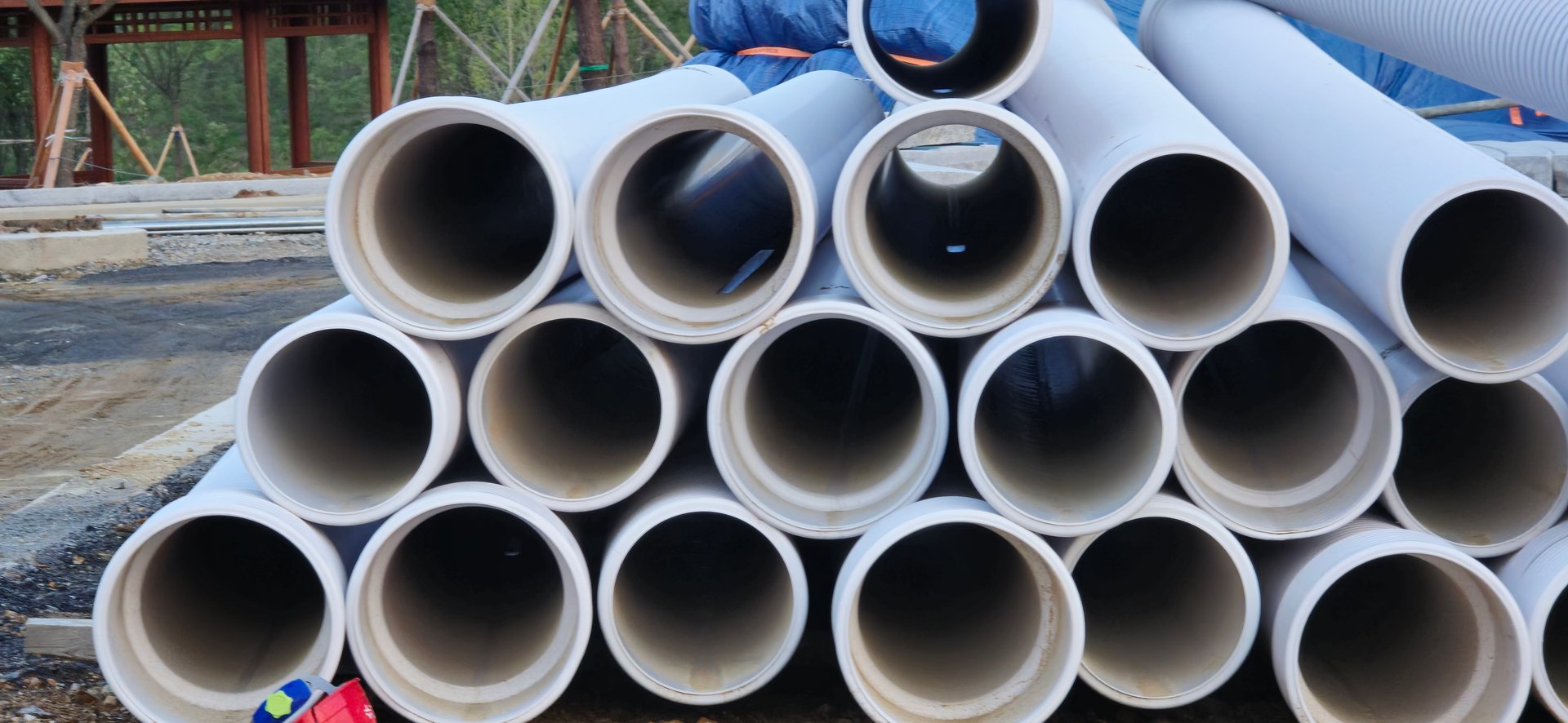 White plastic pipes for water infrastructure. Stacked PVC or HDPE pipes at a construction site for plumbing, drainage, or utility lines.