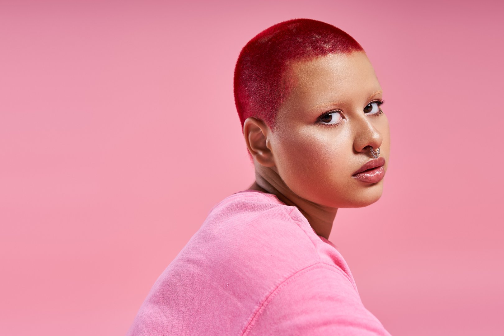 This vibrant young woman showcases her striking pink hairstyle and bold fashion in a chic studio environment.