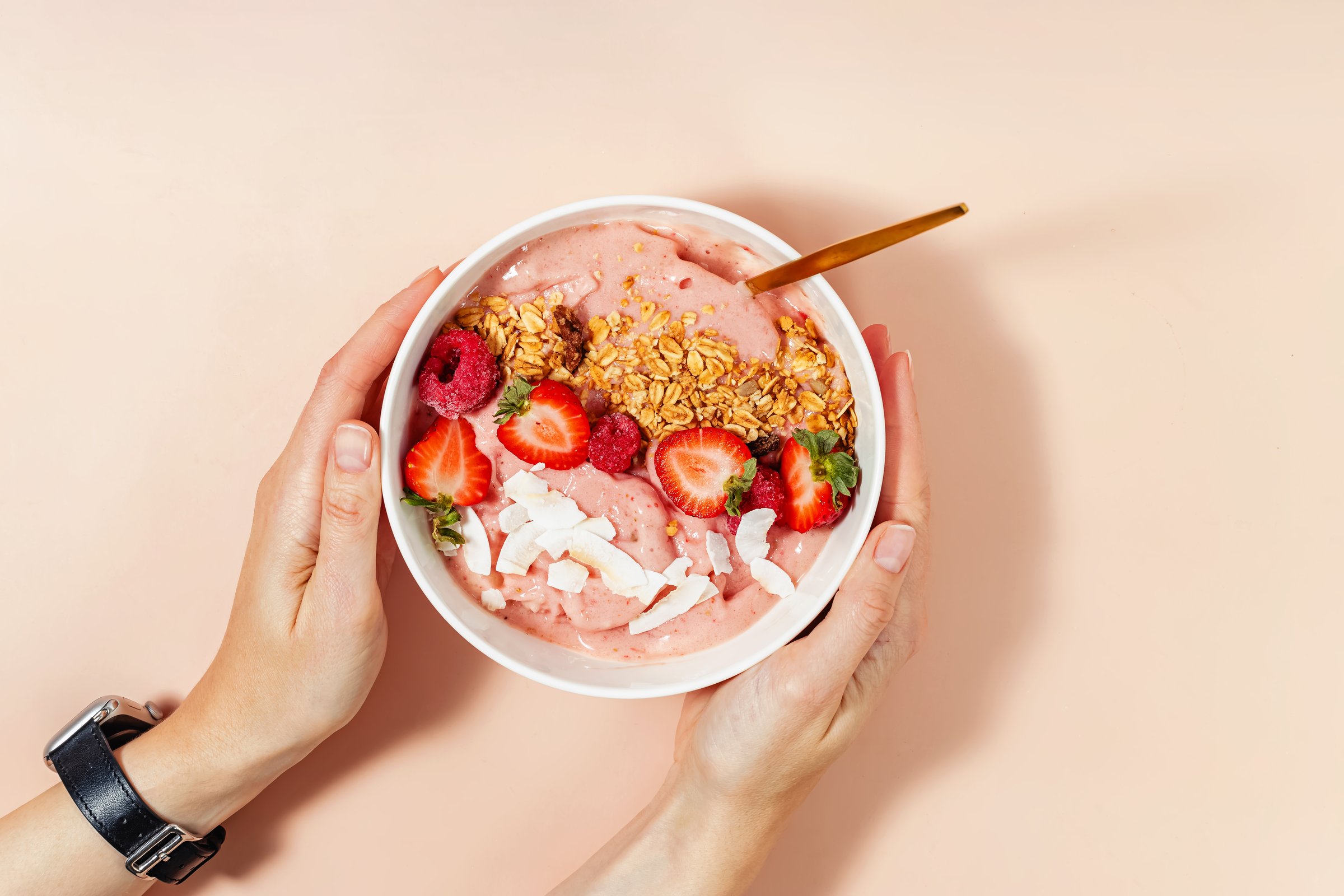 Hand holding a vibrant smoothie bowl, topped with strawberries, raspberries and granola