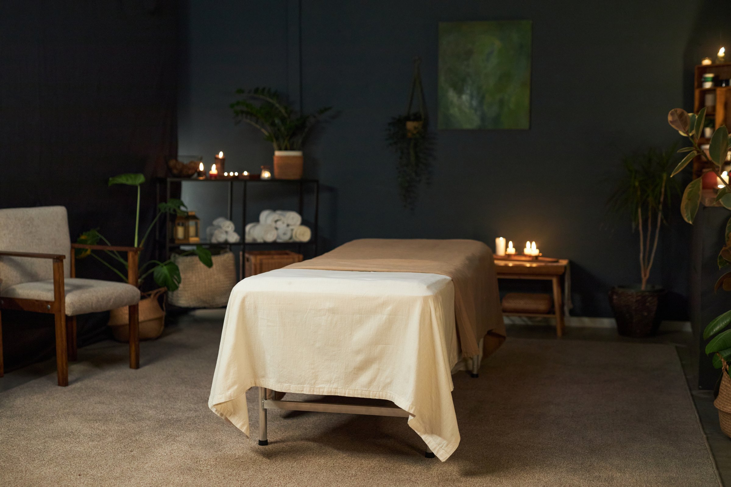 Relaxing massage table setup in a tranquil room setting with candles, plants, and comfortable seating creating a peaceful and soothing atmosphere
