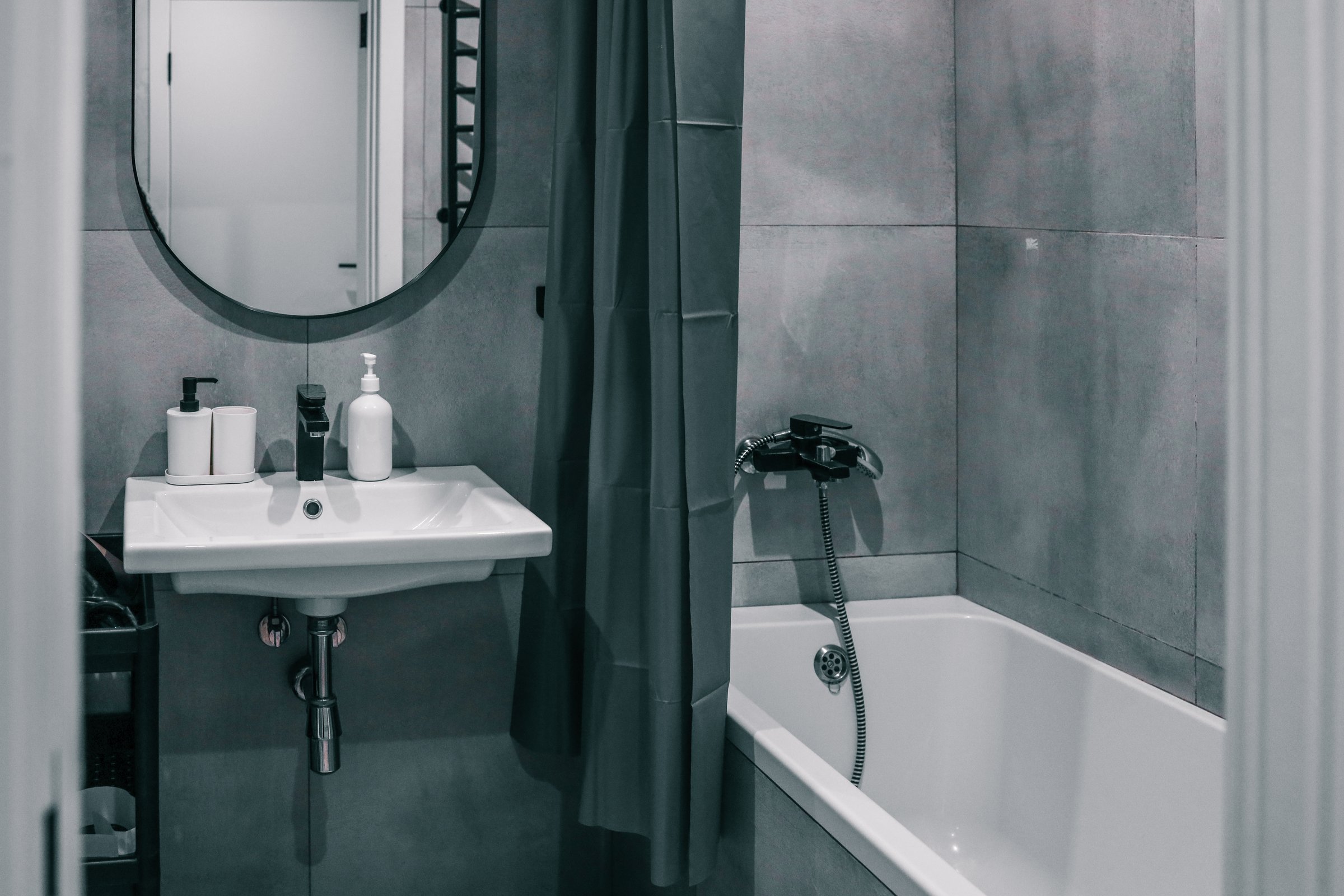 Modern bathroom with minimalistic design, featuring a white sink, wall-mounted mirror, gray shower curtain, and tiled walls. Clean and compact interior setup.