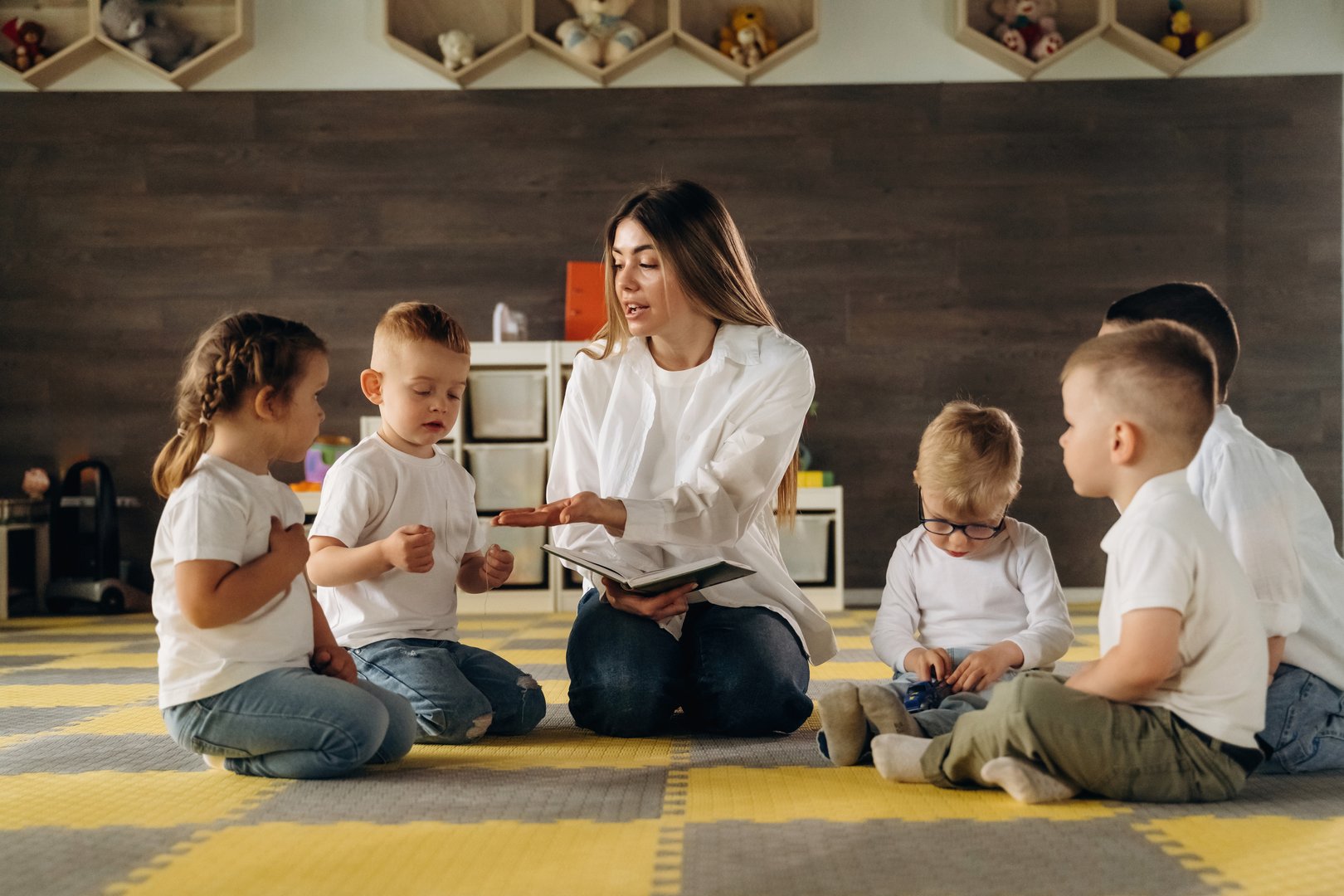 With book, sitting on the floor. Children in kindergarten with their teacher.