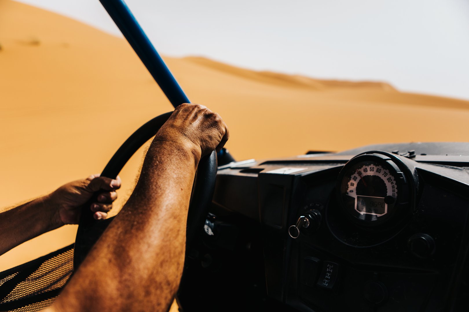 Man hands driving a buggy in the desert dunes viewed from the cockpit.